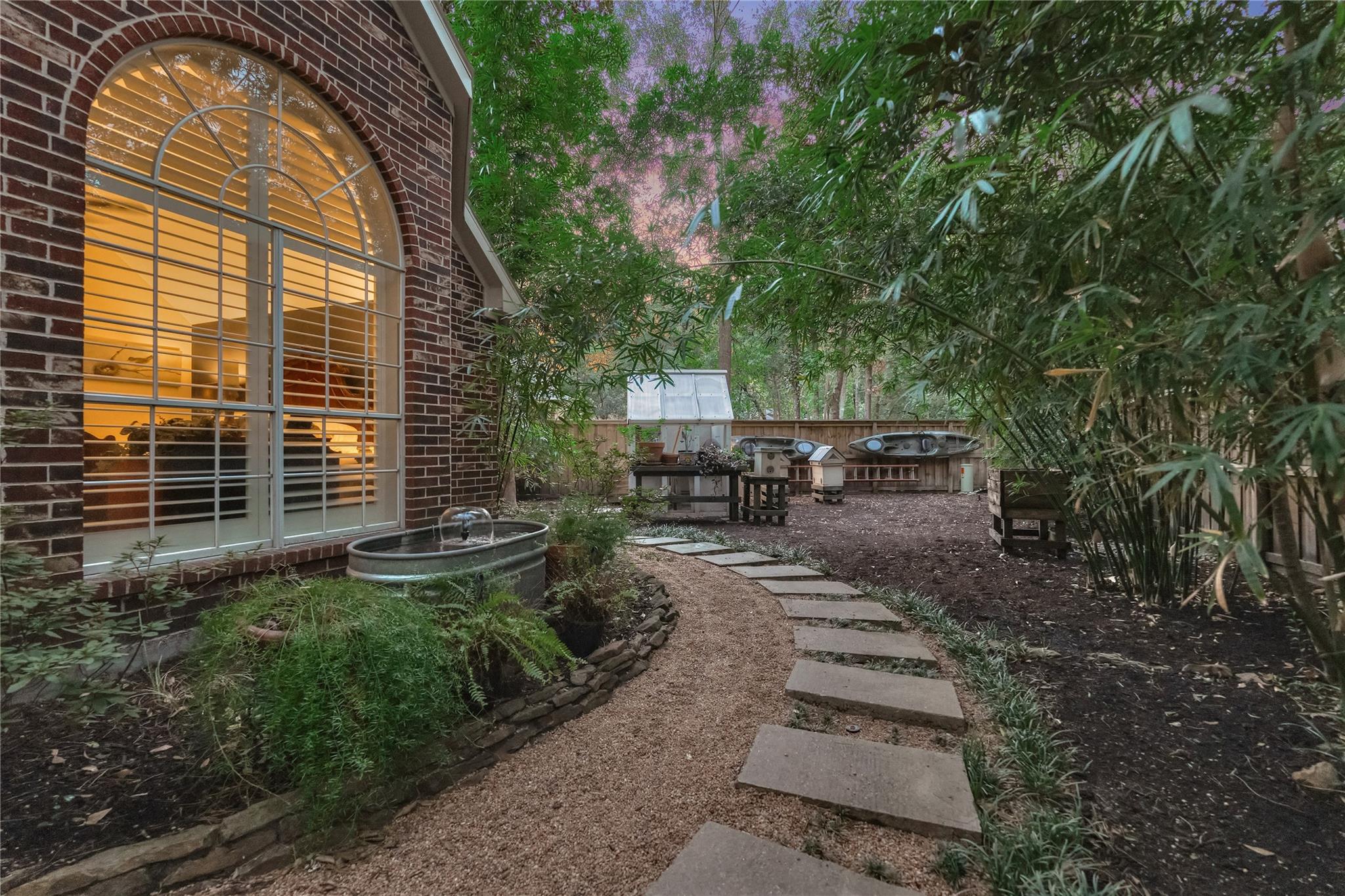 Landscaped backyard with a stepping-stone path, bamboo, beehives, and a glowing arched window.