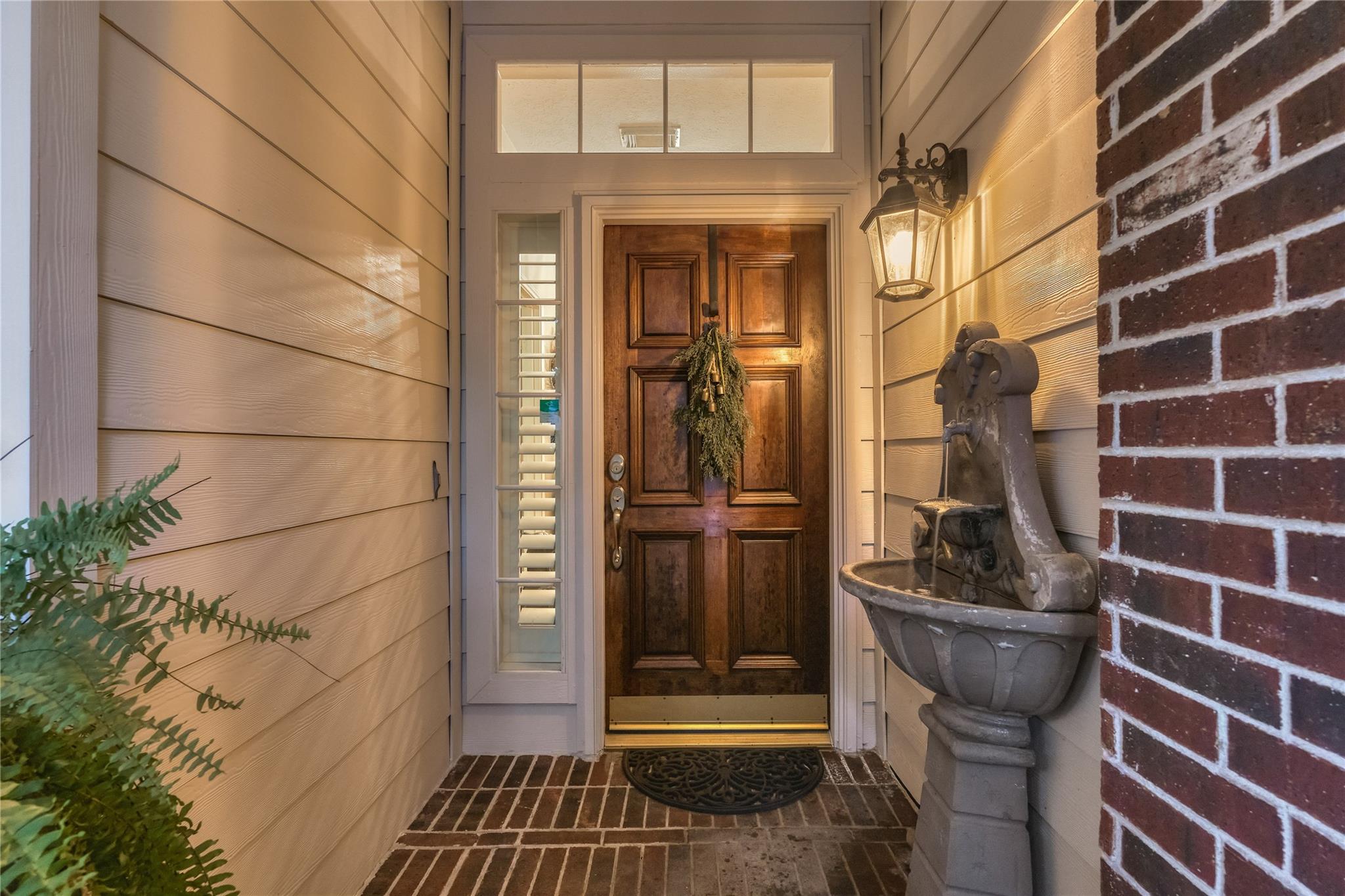Home’s front entry with a paneled wood door, brick porch, and stone fountain.
