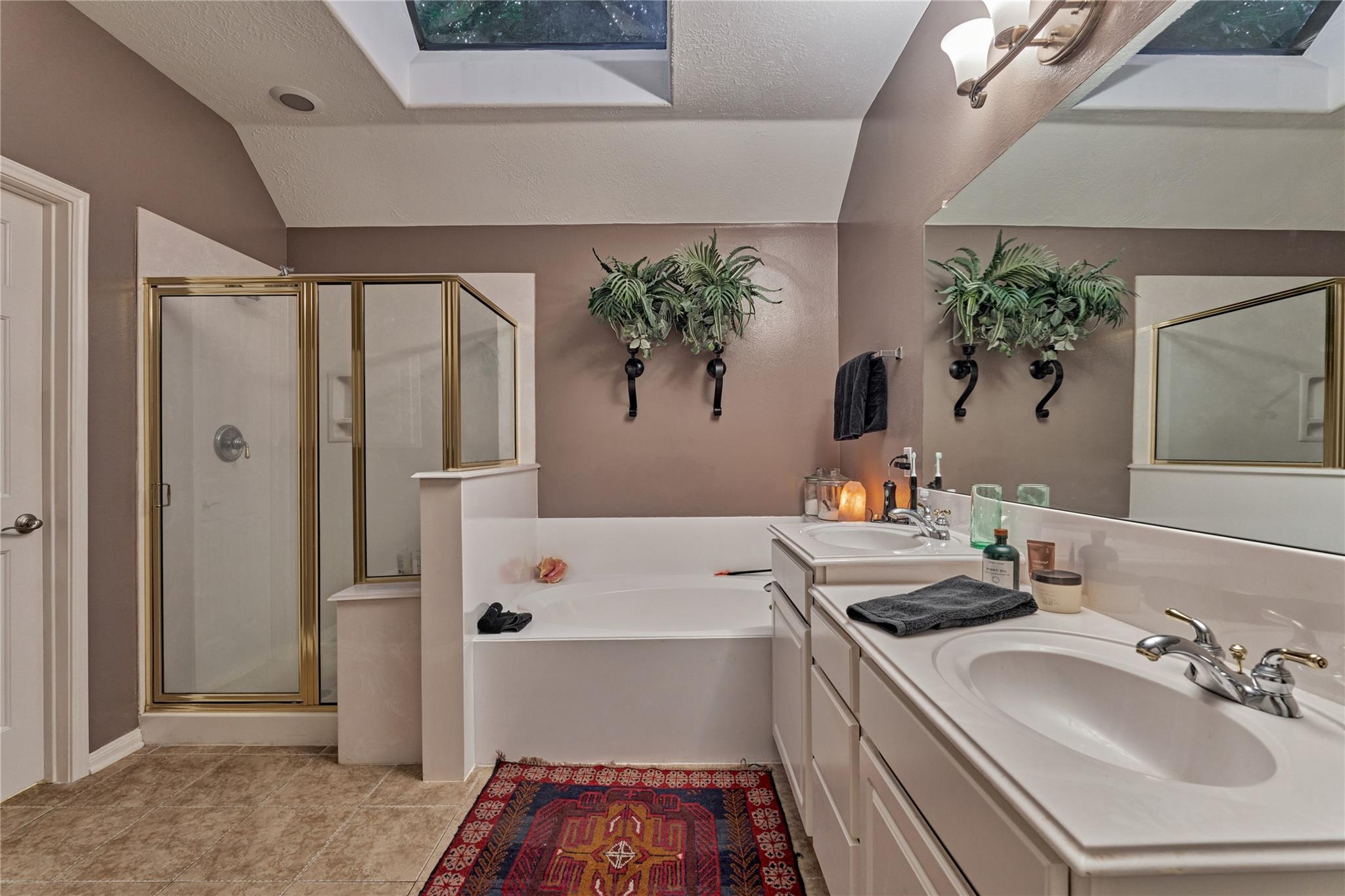 Bathroom with a built-in soaking tub, brass-trimmed shower, and double vanity beneath a large mirror.