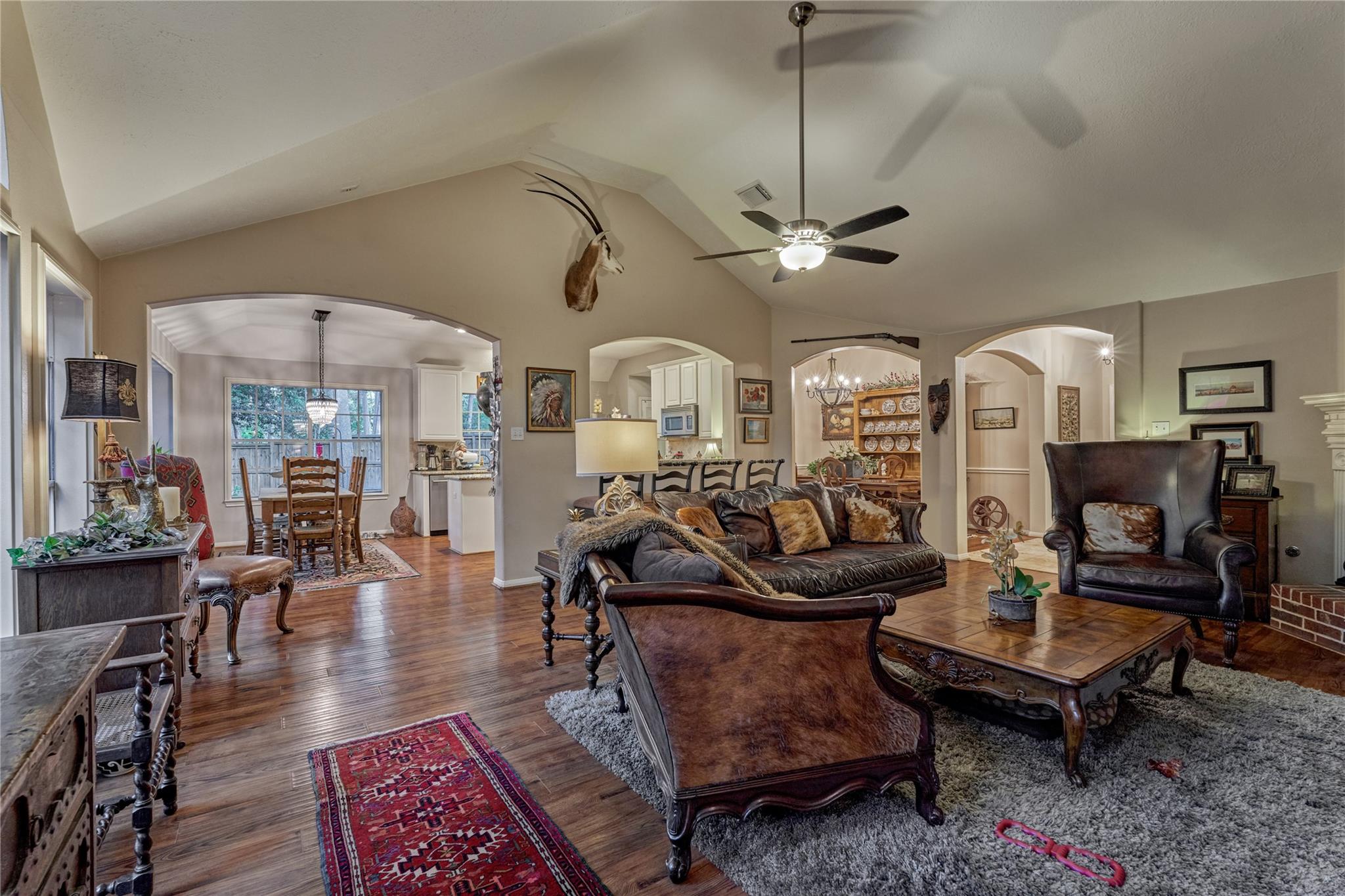 Living room with vaulted ceiling, hardwood floors, leather seating, and arched openings to the dining area and kitchen.
