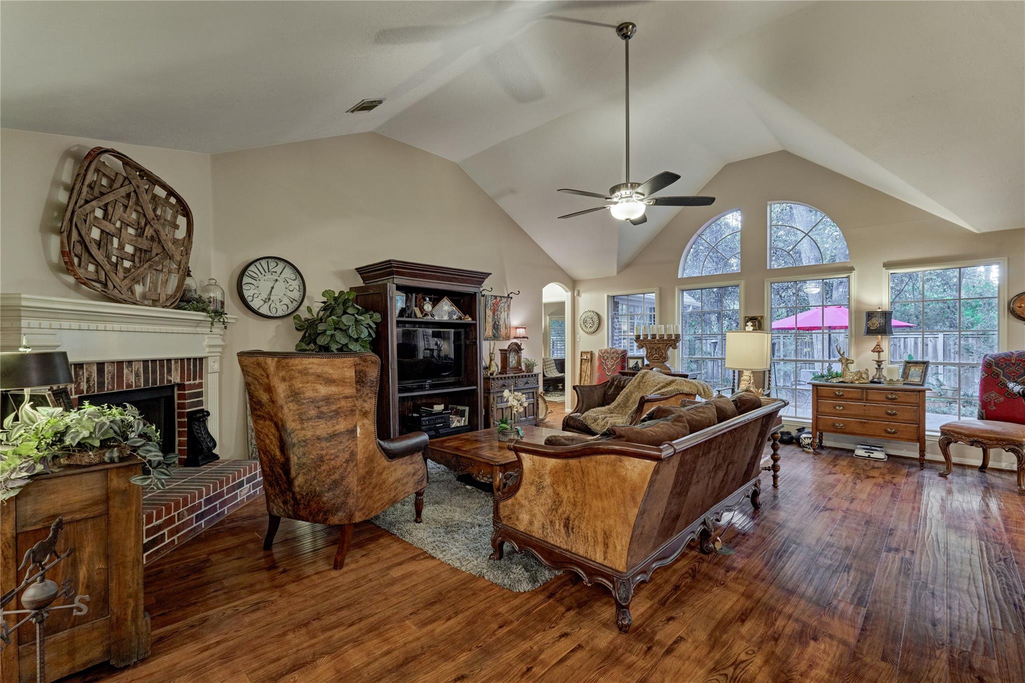 Living room with a brick fireplace, vaulted ceiling, and tall arched windows.