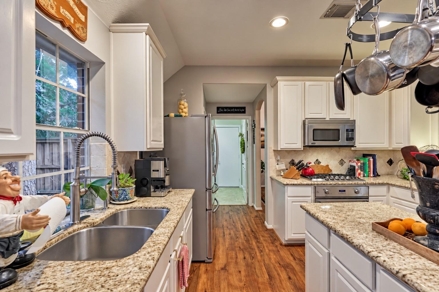 Kitchen with white cabinets, granite counters, stainless appliances, and a double-basin sink beneath a window.