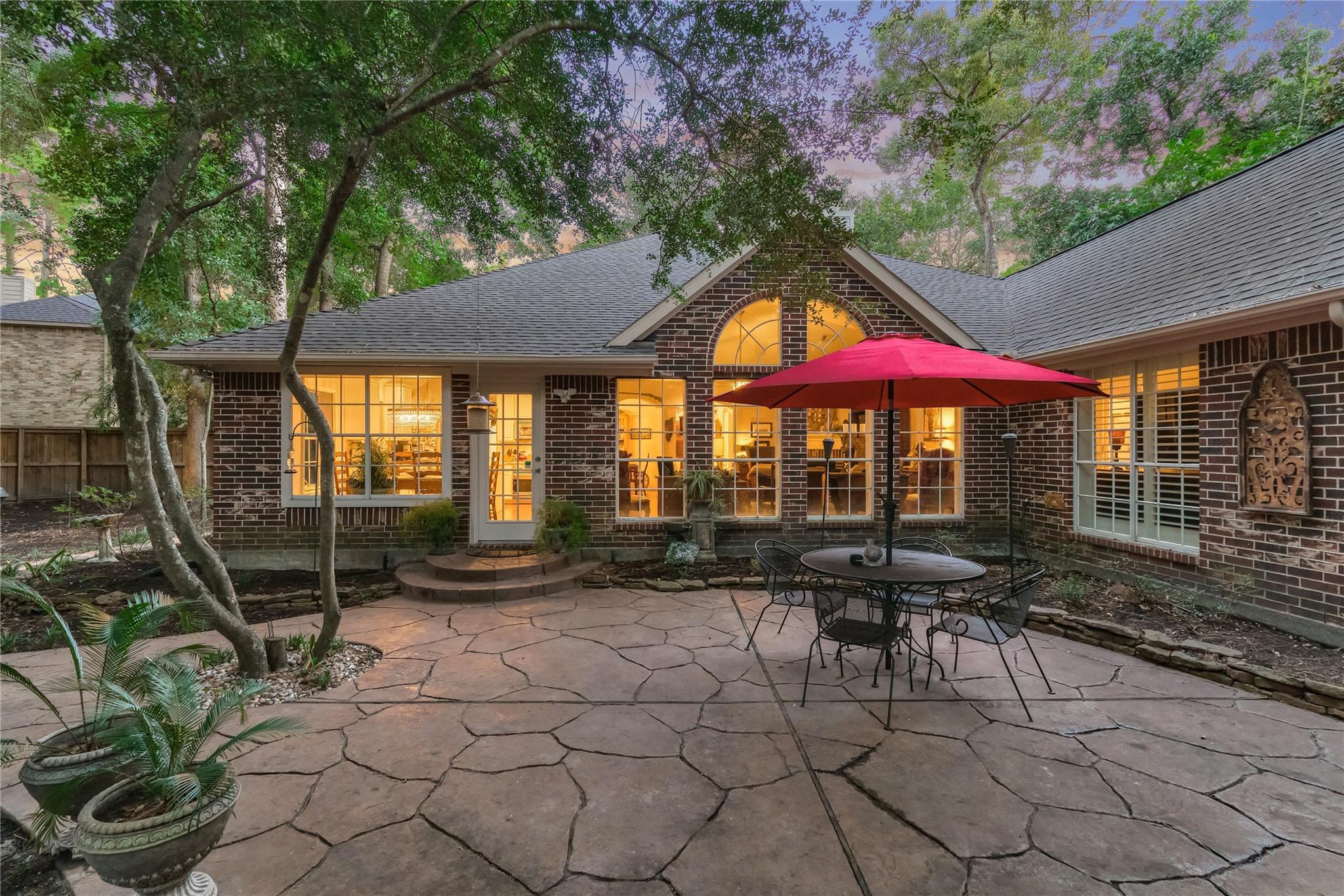 Brick home’s rear patio at dusk, with glowing windows and a dining set beneath a red umbrella.