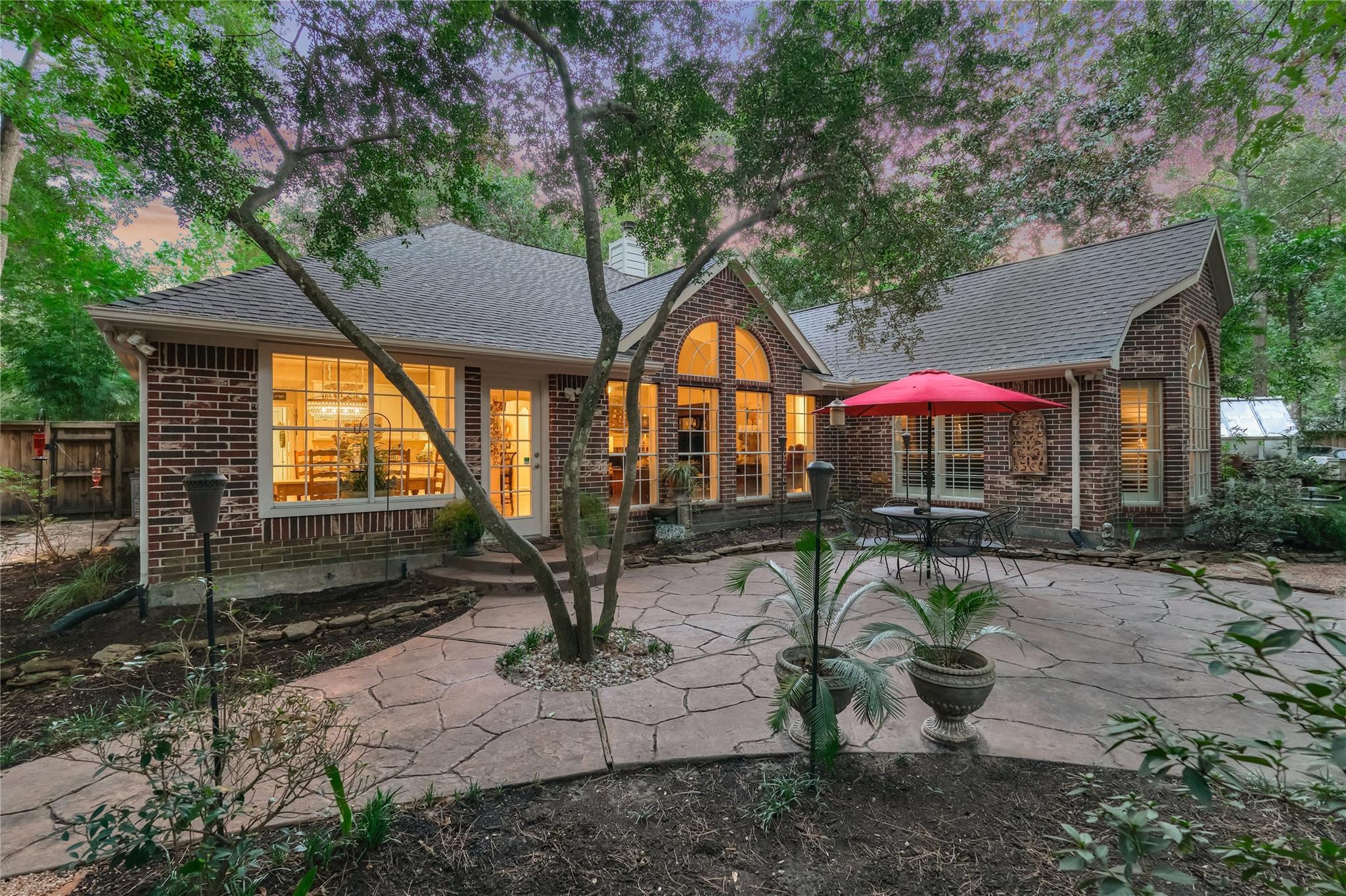 Brick home with arched windows and a flagstone patio beneath mature trees at dusk.