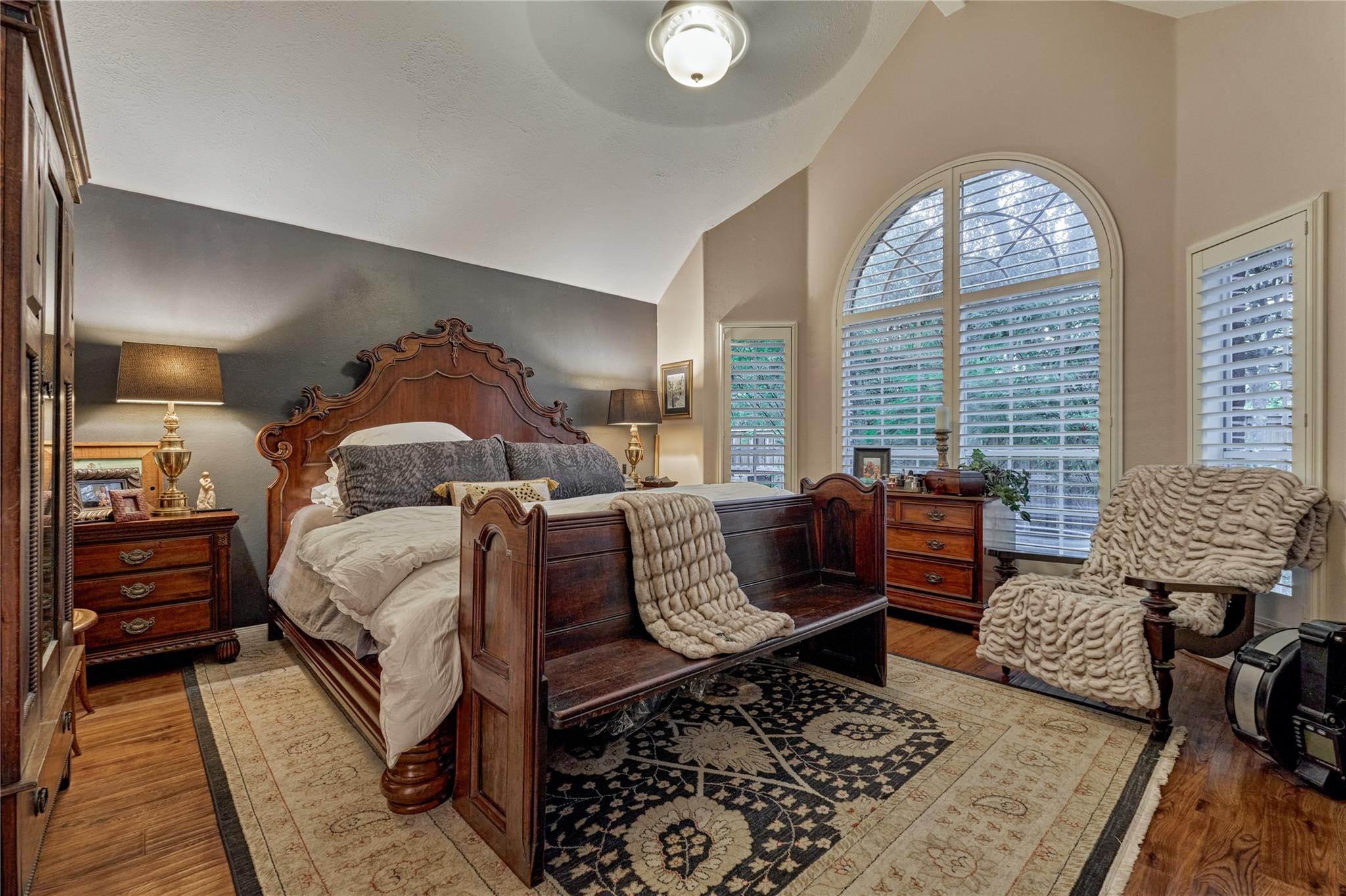 Bedroom with an ornate wooden bed, large arched window, and layered patterned rugs.