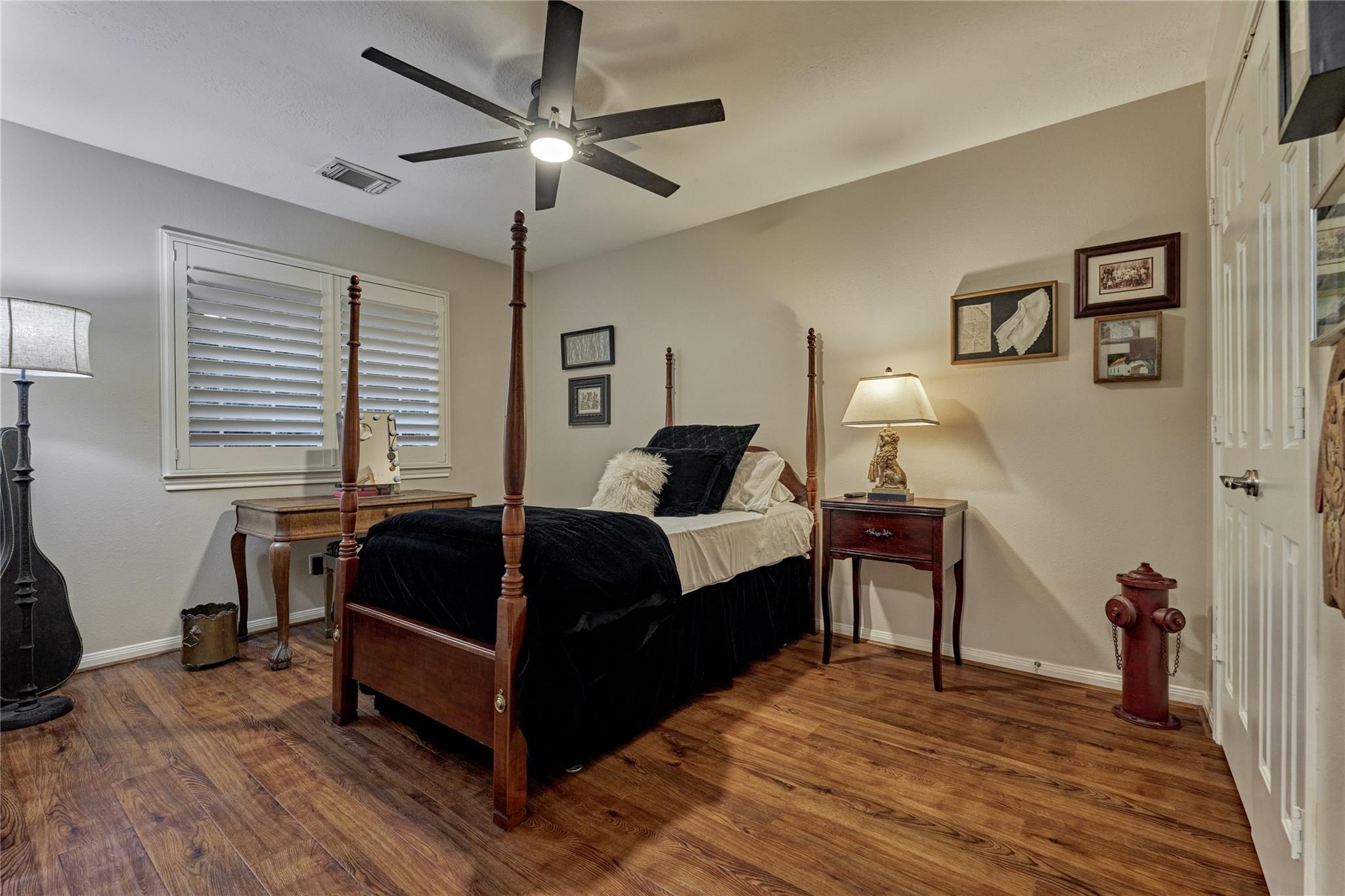 Bedroom with a dark four-poster bed, plantation shutters, wood-look flooring, and a red fire hydrant.