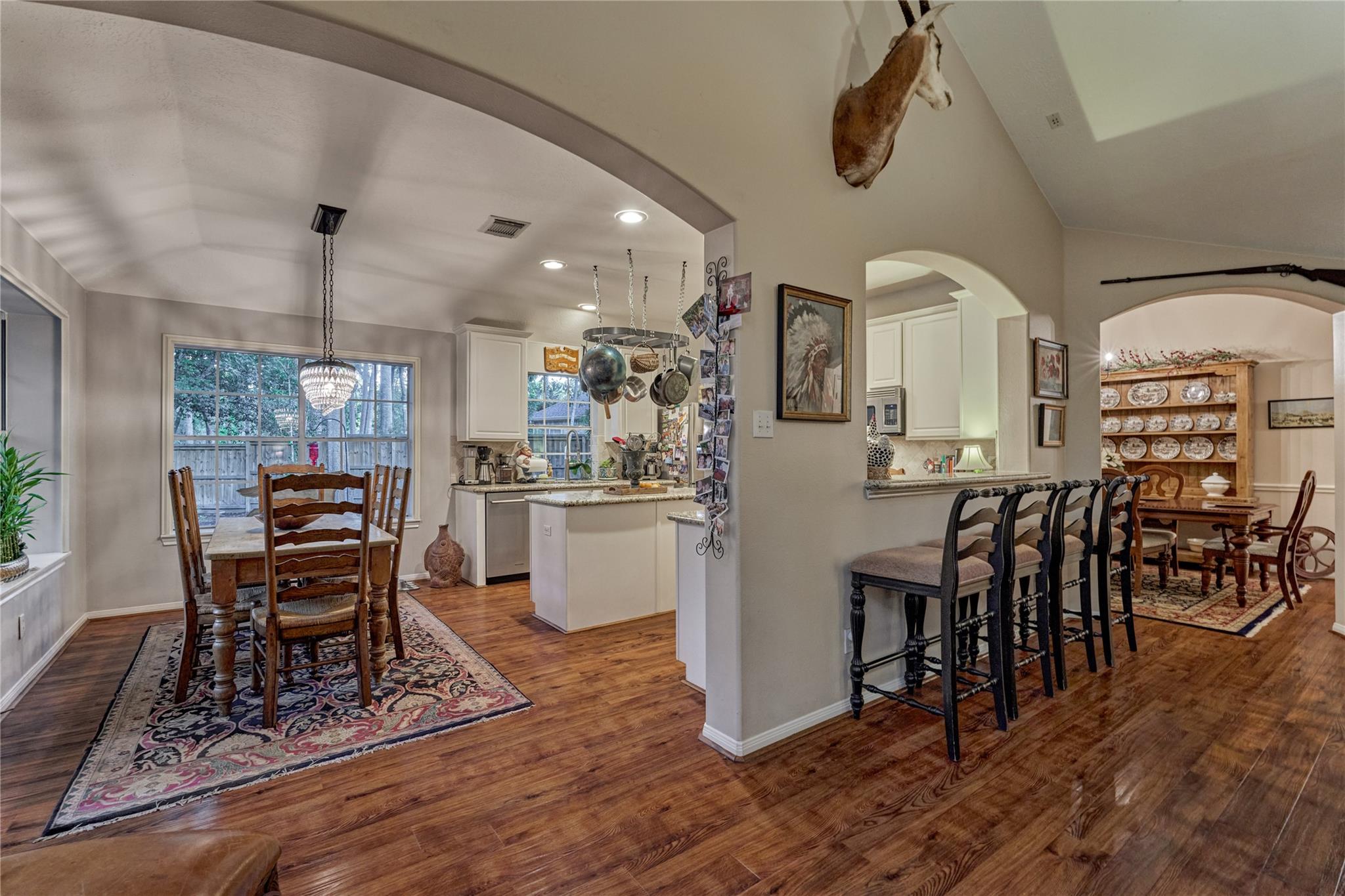 Open-plan kitchen and dining area with wood floors, white cabinetry, and a long row of bar stools.