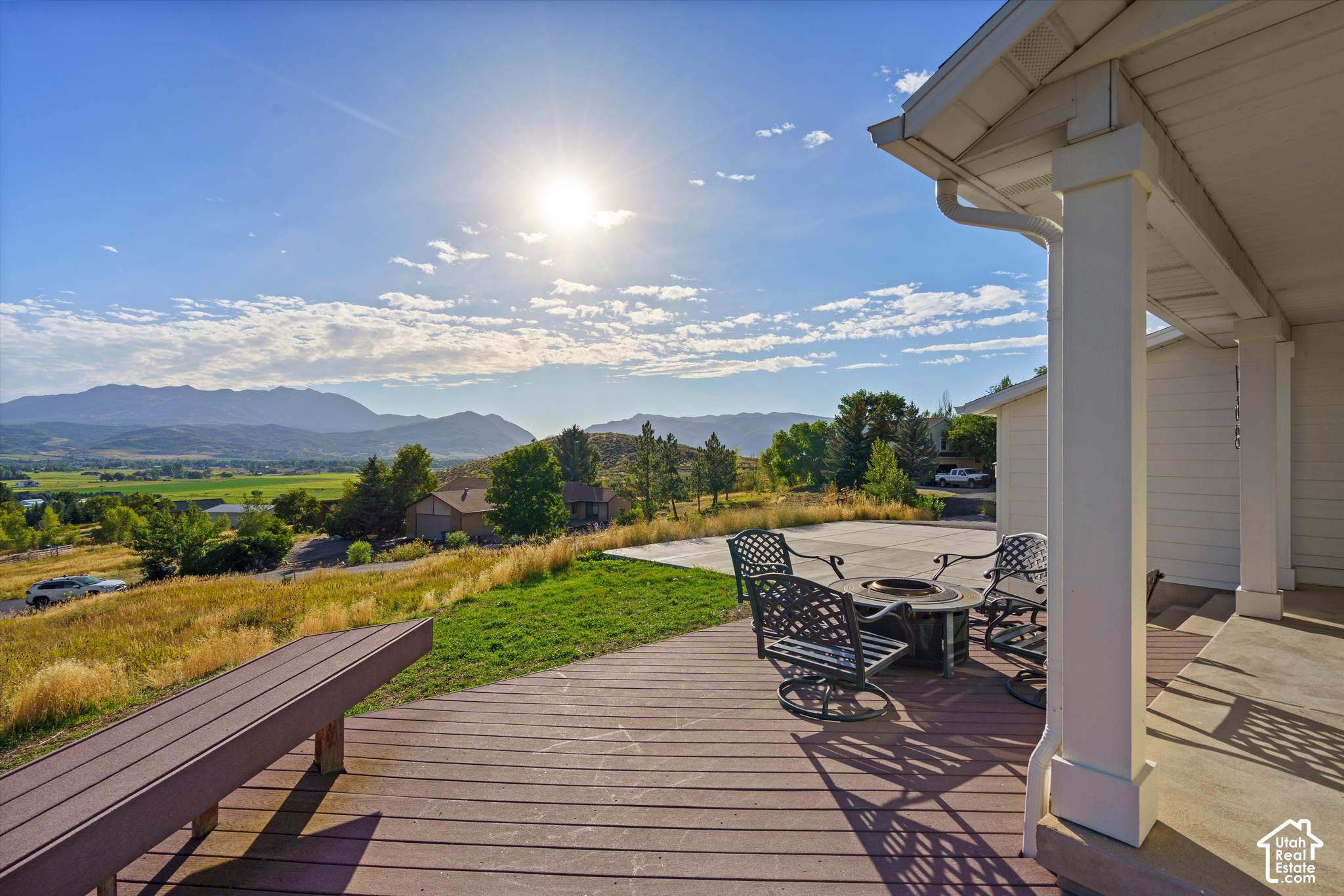 Covered wooden deck with patio seating and a fire pit overlooking a valley and mountains.