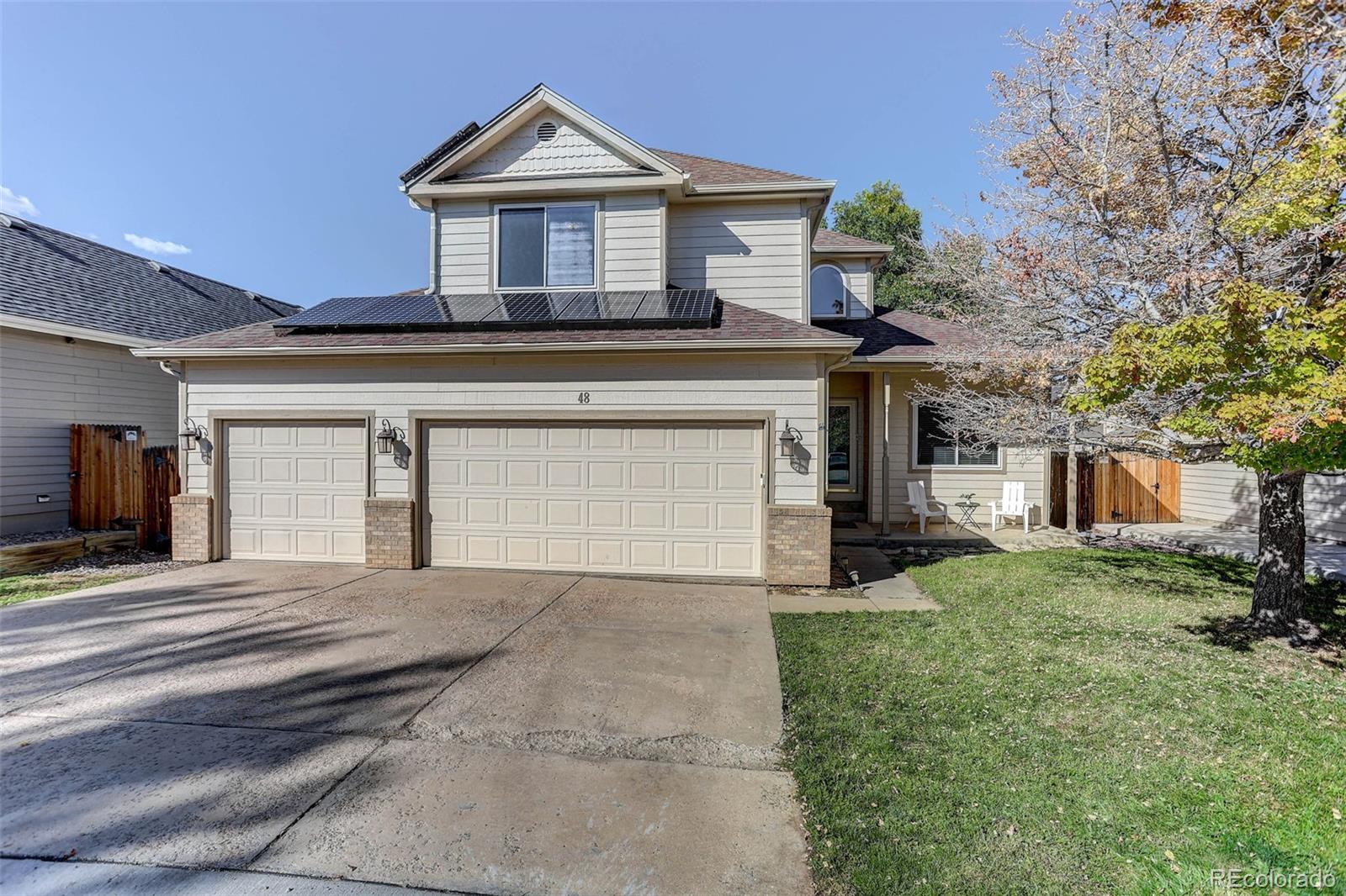 Two-story gray house with rooftop solar panels, a three-car garage, and a front lawn.