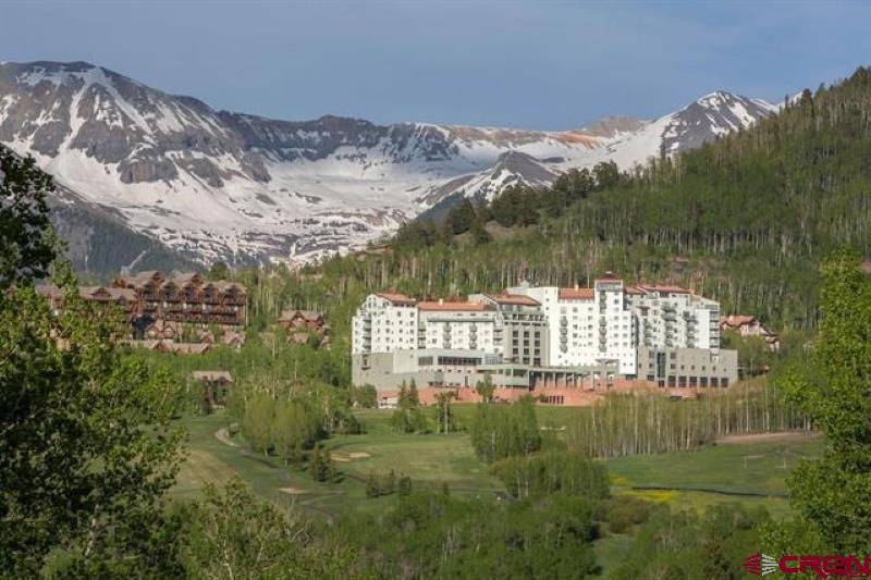 Mountain resort complex with green grounds, forested slopes, and snow-streaked peaks.