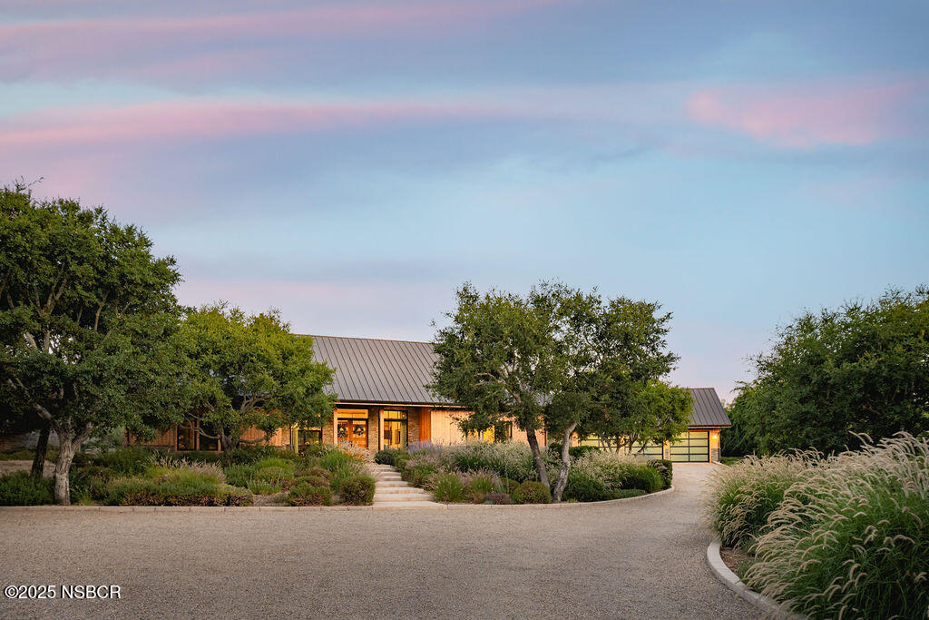Single-story home with a dark metal roof, warm wood siding, and a curved gravel driveway.