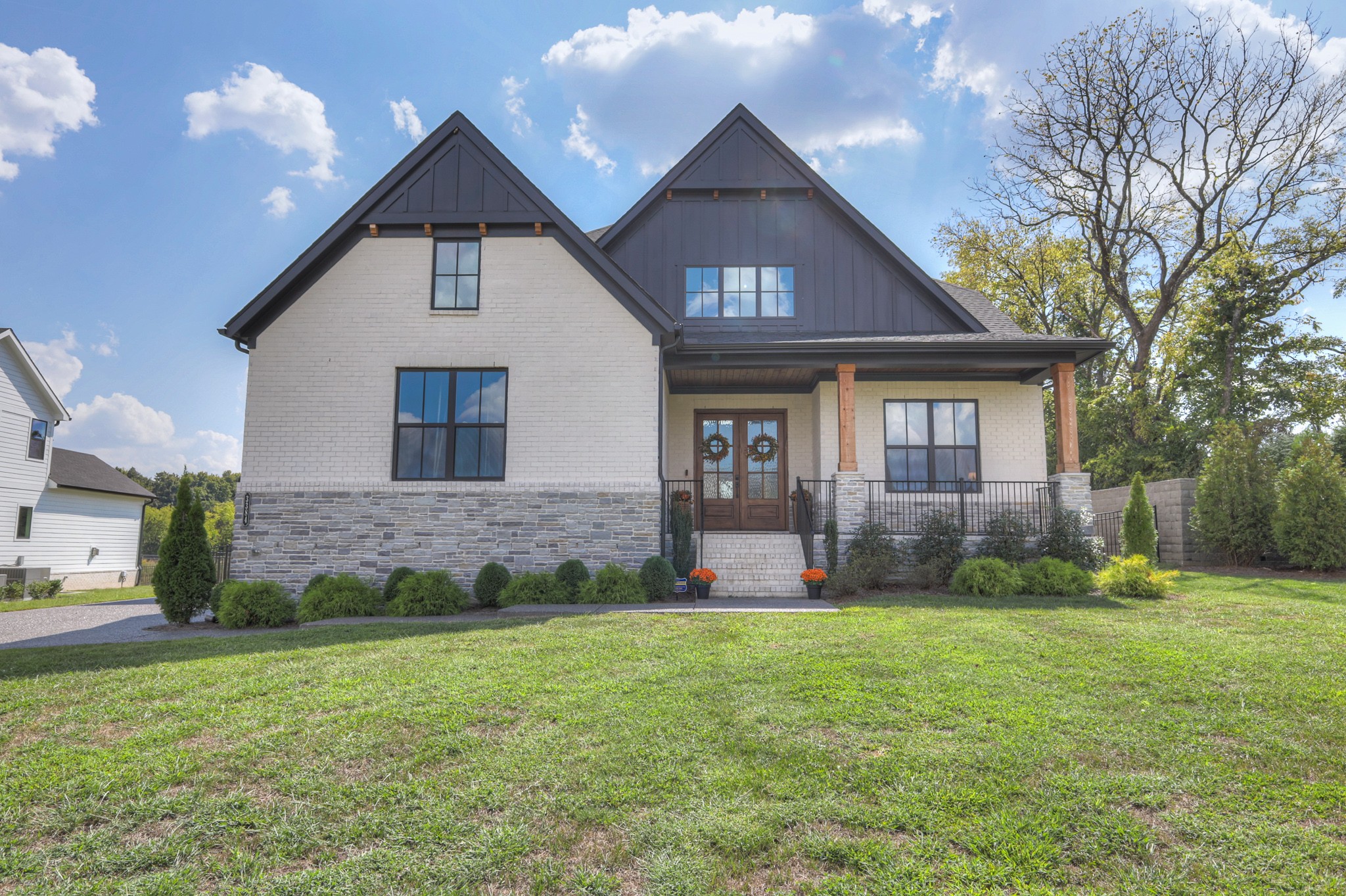 White brick home with a stone foundation, dark gabled roof, and covered porch behind a green lawn.