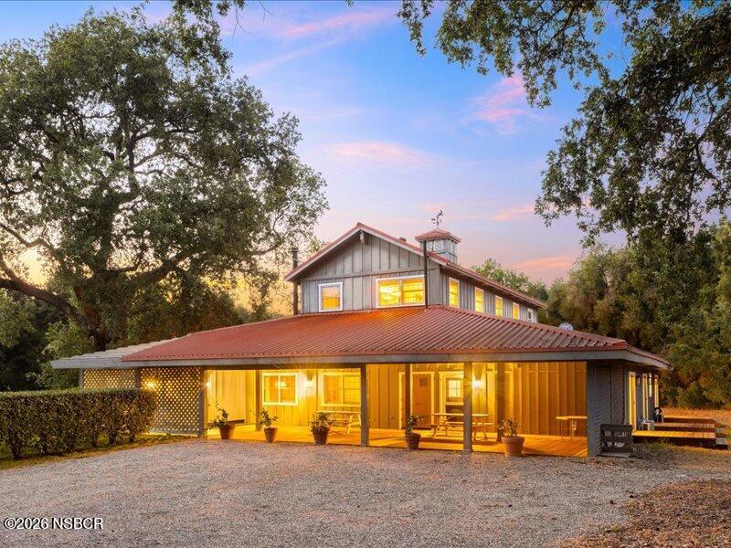 Two-story wood-sided home with an illuminated covered porch and red metal roof at dusk.