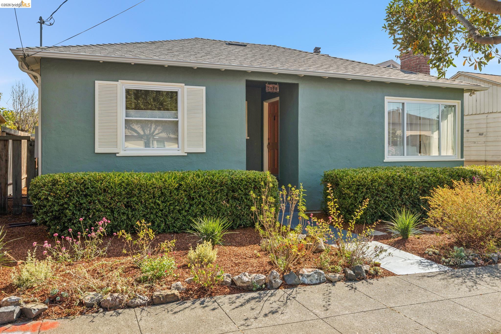 Teal single-story house with a recessed wooden door and landscaped front garden.
