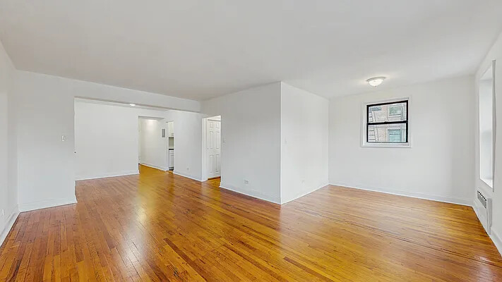 Vacant living room with polished hardwood floors and an opening to the hallway.