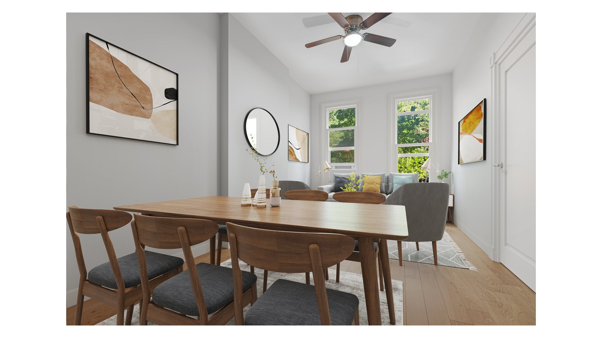 Dining and living area with a wooden table, gray sofa, and tall windows overlooking leafy trees.
