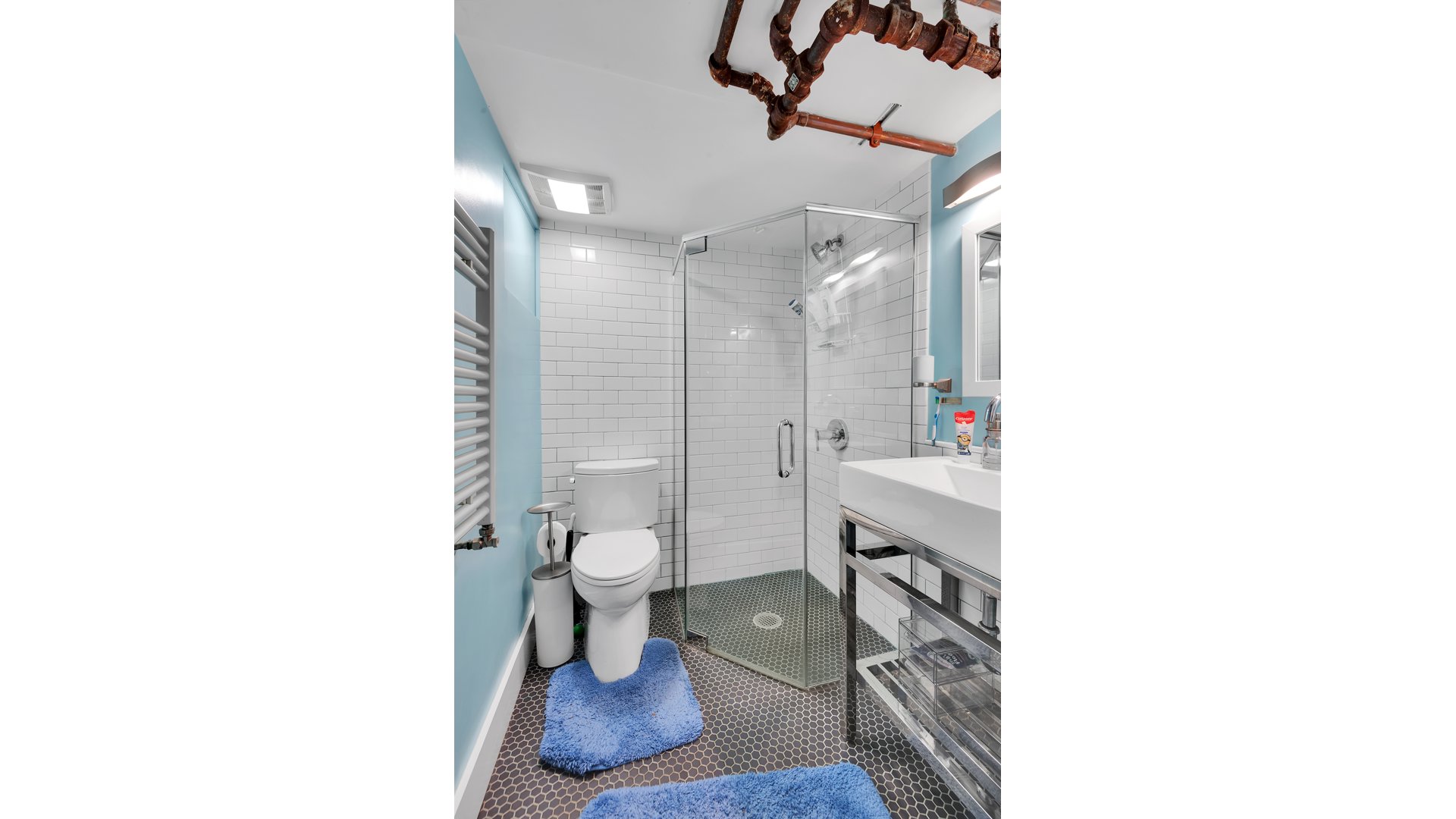 Bathroom with glass walk-in shower, white subway tile, blue walls, and exposed ceiling pipes.
