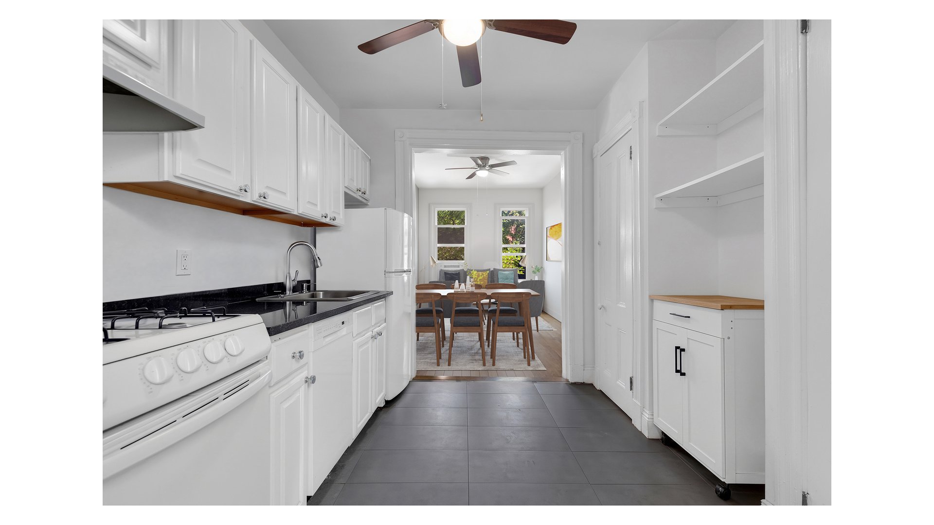 White kitchen with dark counters and gray tile opens to a dining area with a wooden table.