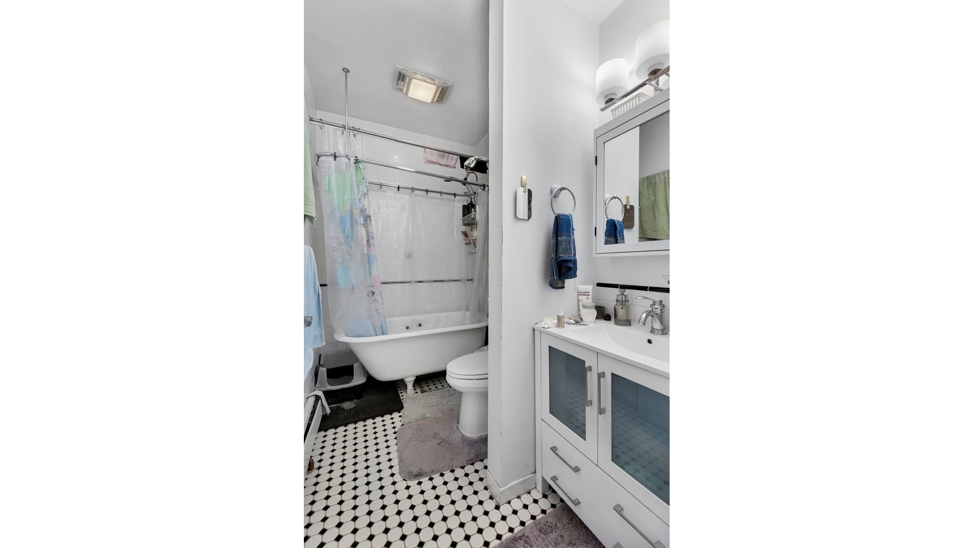 Bathroom with a clawfoot tub, mirrored vanity, and black-and-white hexagonal floor tiles.
