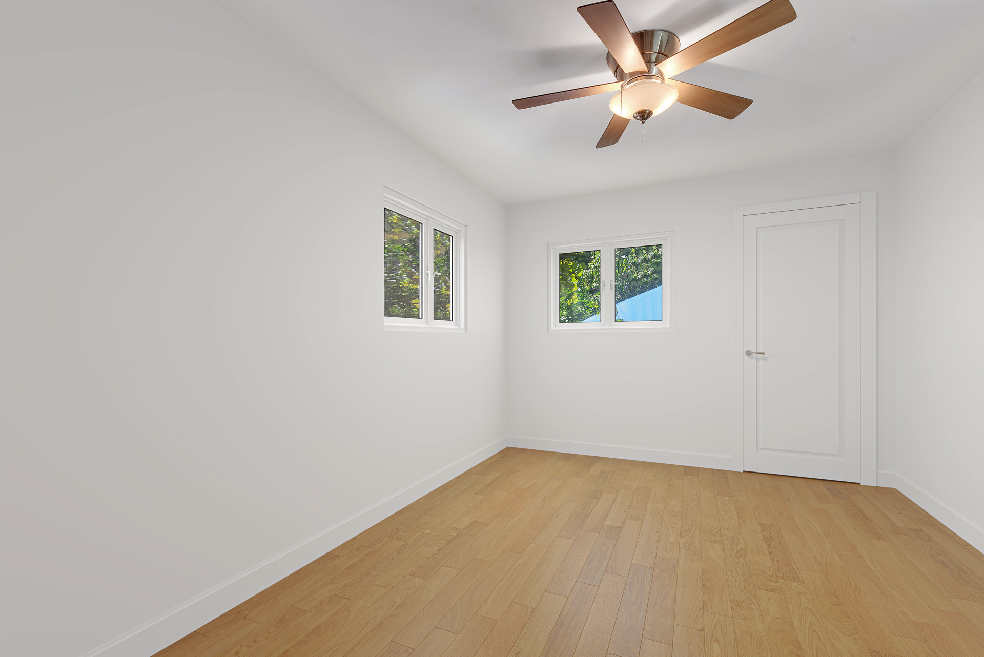 Vacant bedroom with hardwood floors, two windows, and a ceiling fan with light.