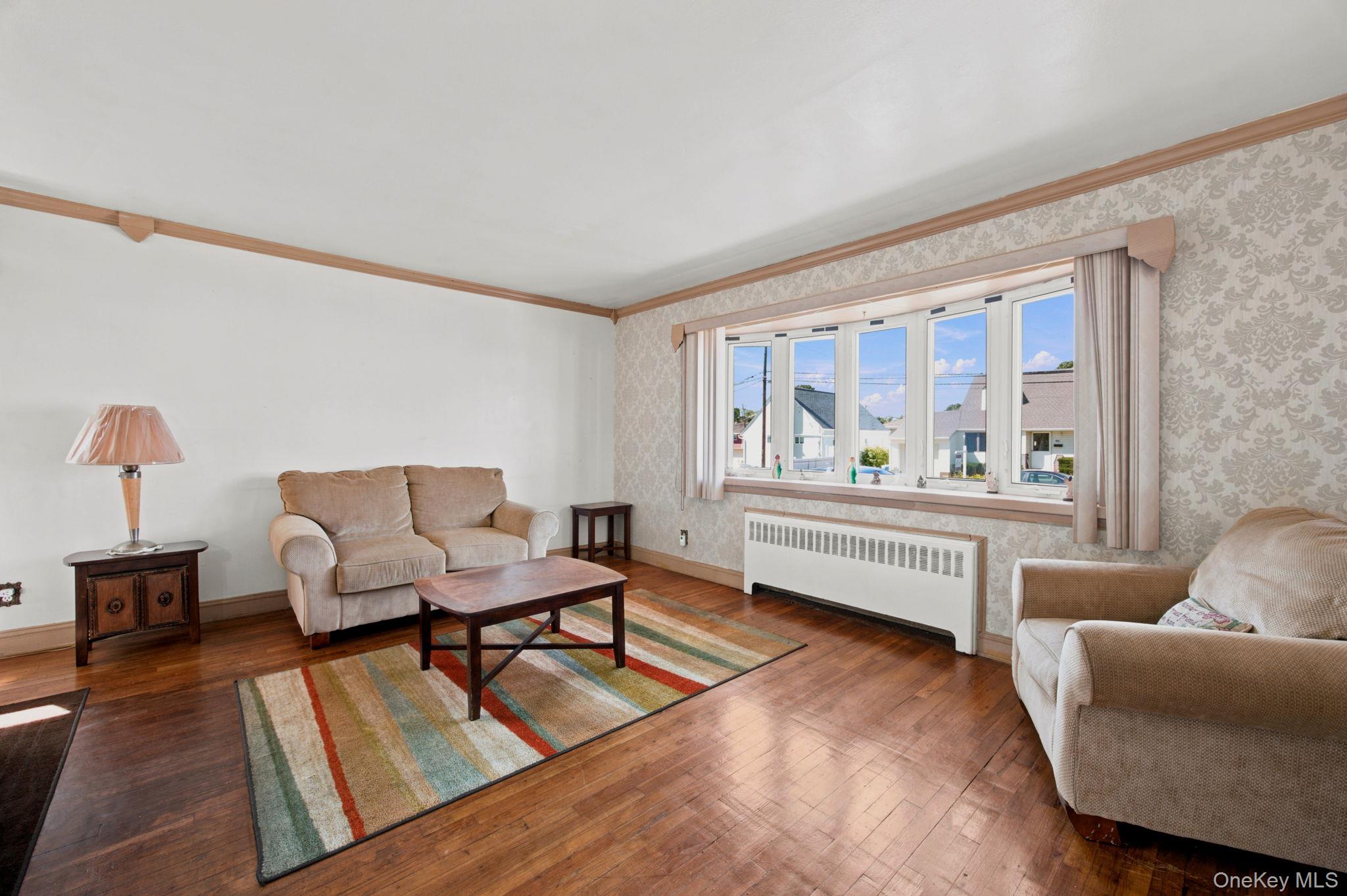 Furnished living room with hardwood floors, beige sofas, and wide windows overlooking neighboring homes.