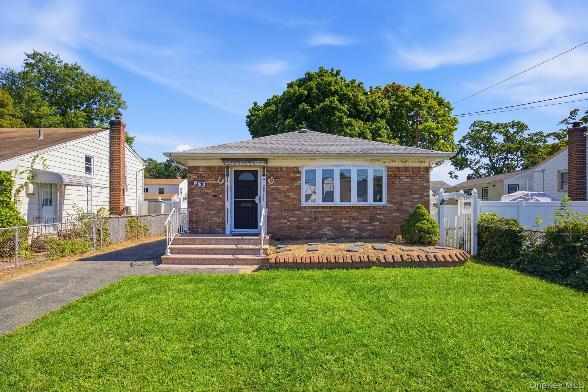 Single-story brick house with a wide front window, front steps, and a large green lawn.