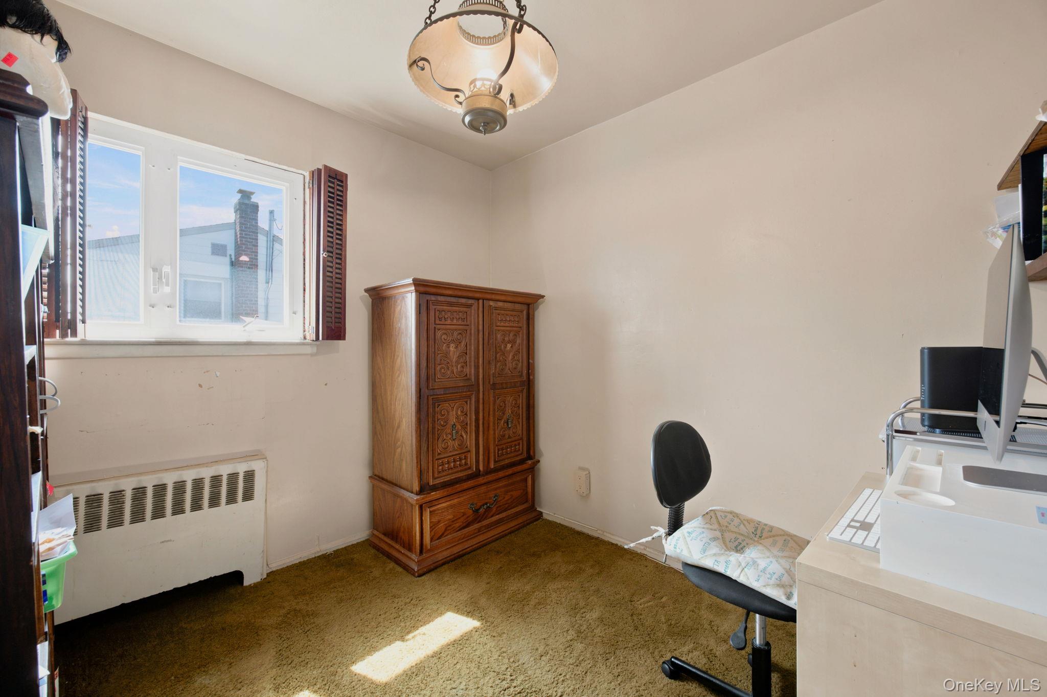 Home office with a carved wooden armoire, computer desk, and window with open shutters.