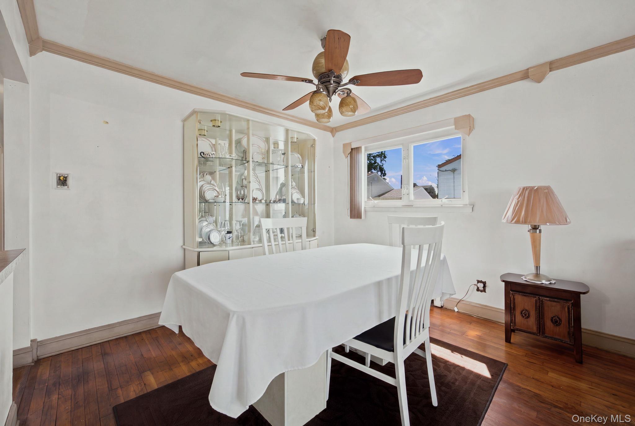 Dining room with a white-covered table, glass china cabinet, and polished hardwood floors.