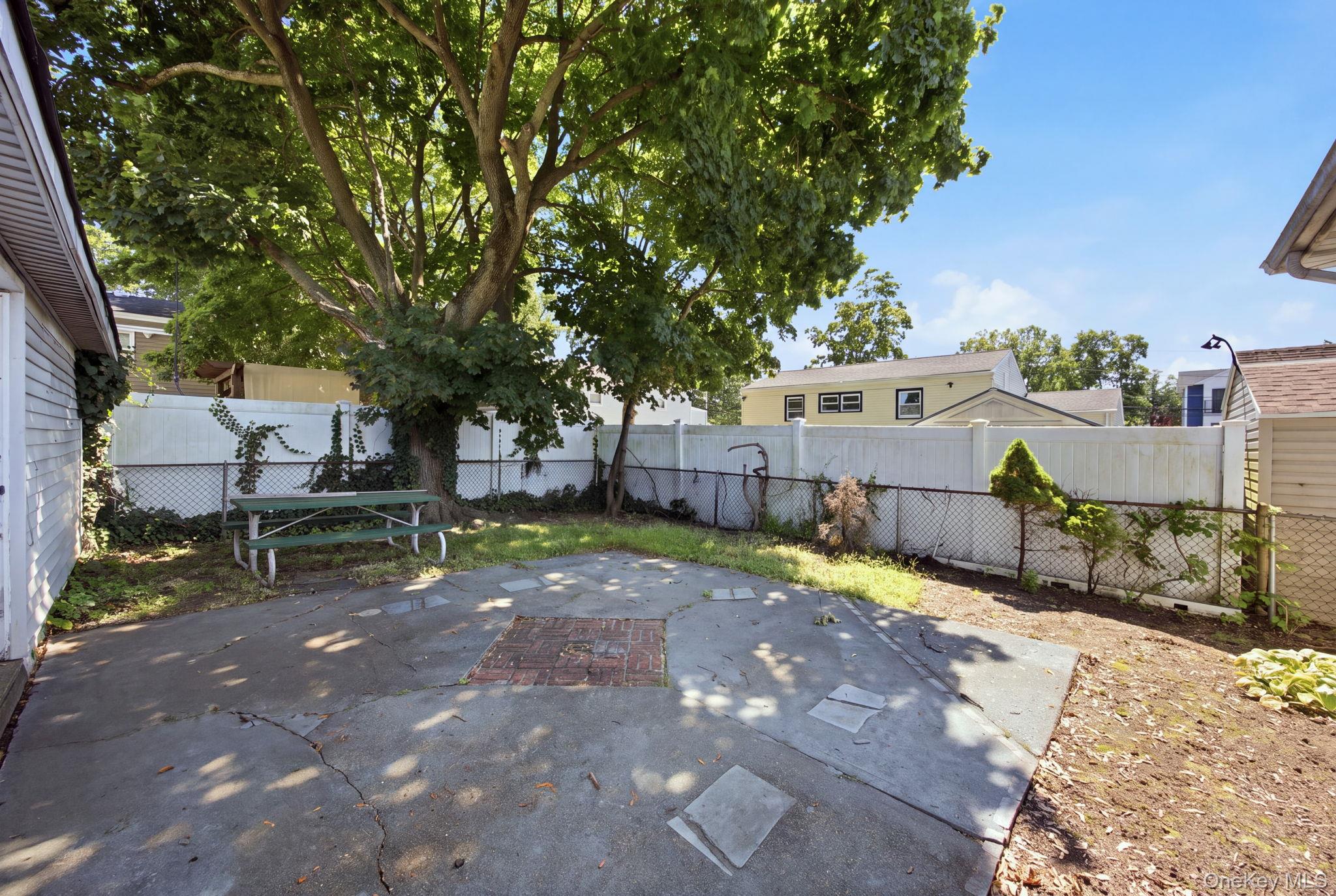 Backyard patio beneath a large shade tree, with a picnic table and fenced yard.