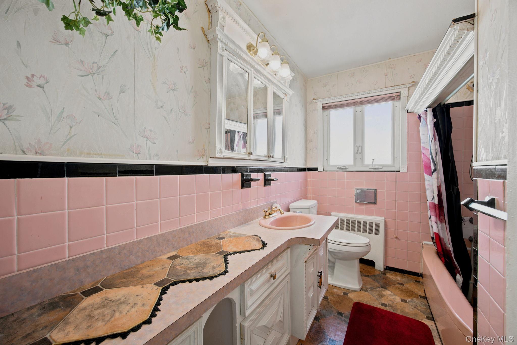 Bathroom with pink tile, floral wallpaper, a long vanity, and a bathtub.
