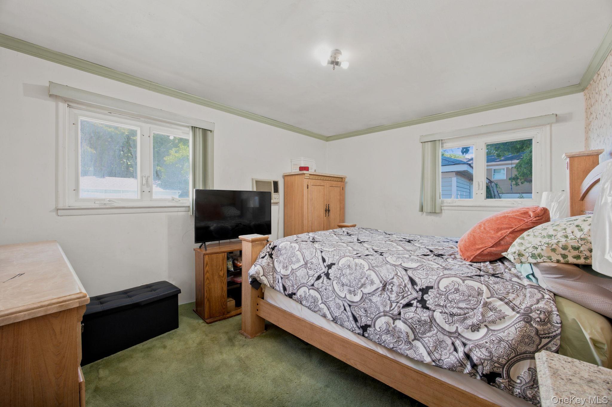 Bedroom with a patterned bedspread, green carpet, two windows, and wooden furniture.