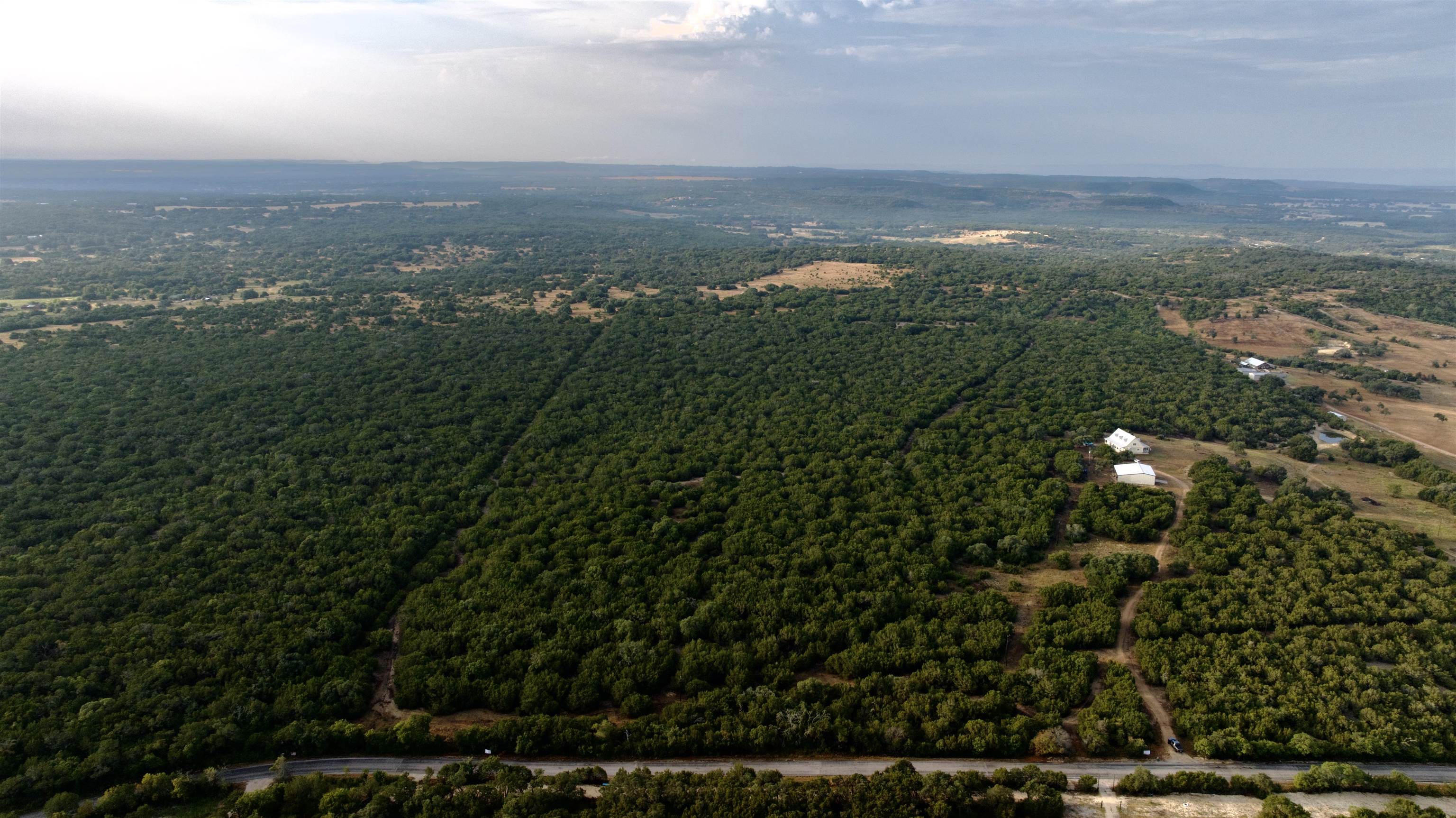 Aerial view of wooded rural acreage with a house and outbuilding beside a road.
