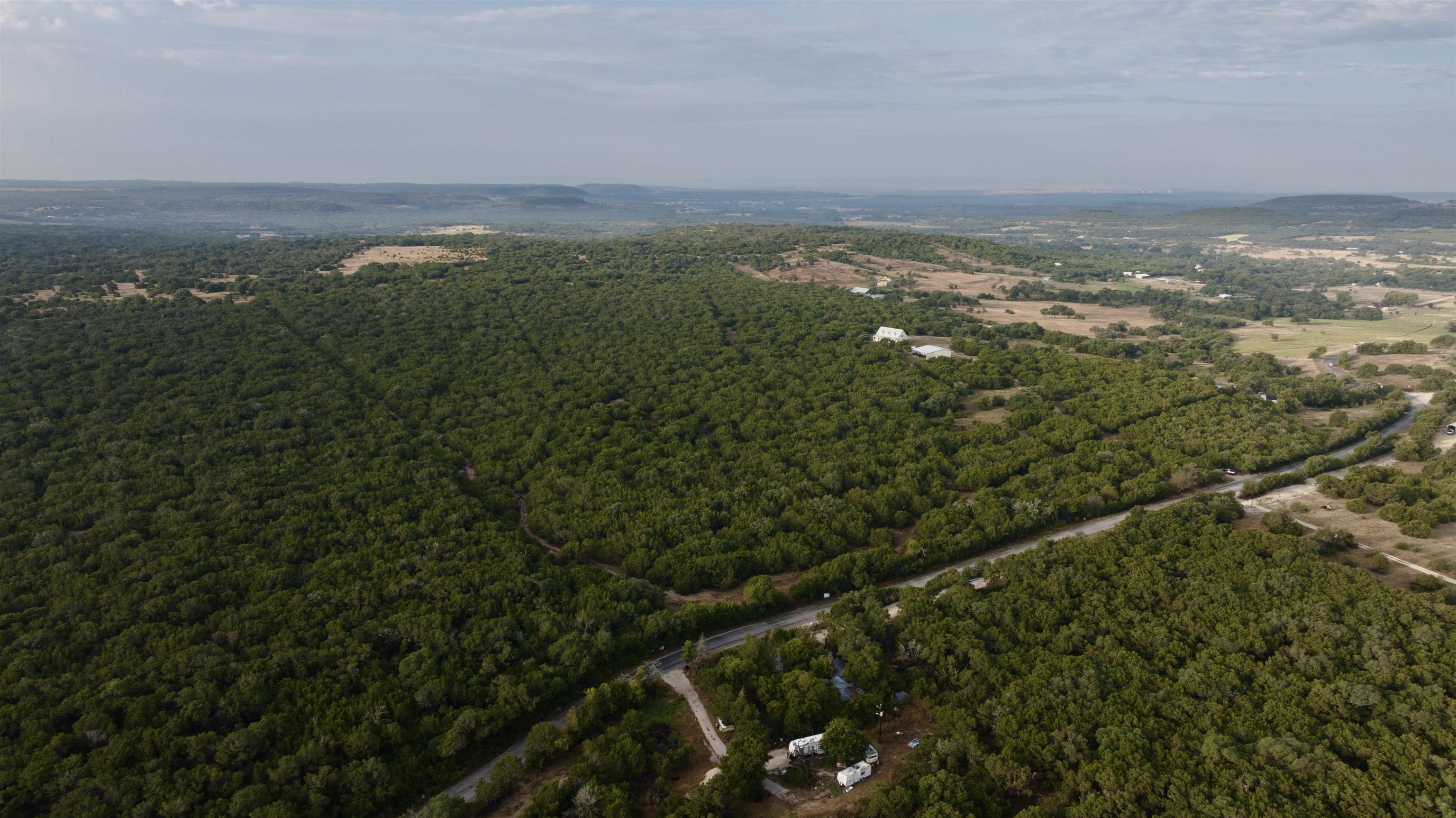 Aerial view of wooded rural land with a curving road and distant hills.