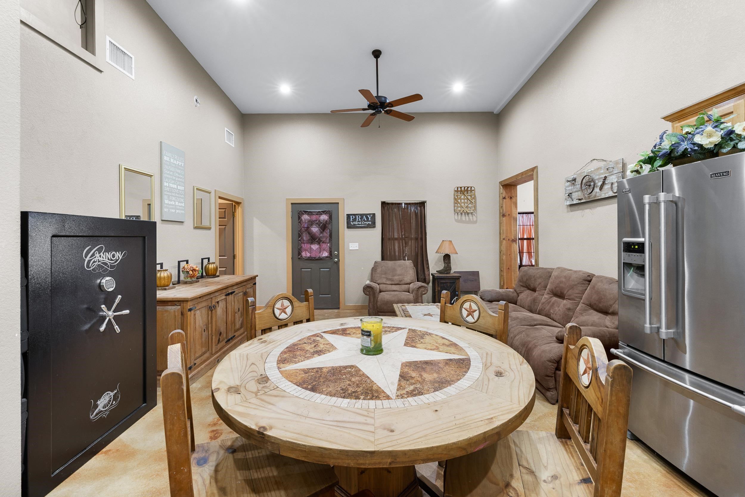 Dining and living area with a round star-inlay table, rustic wooden chairs, brown sofa, and stainless steel refrigerator.
