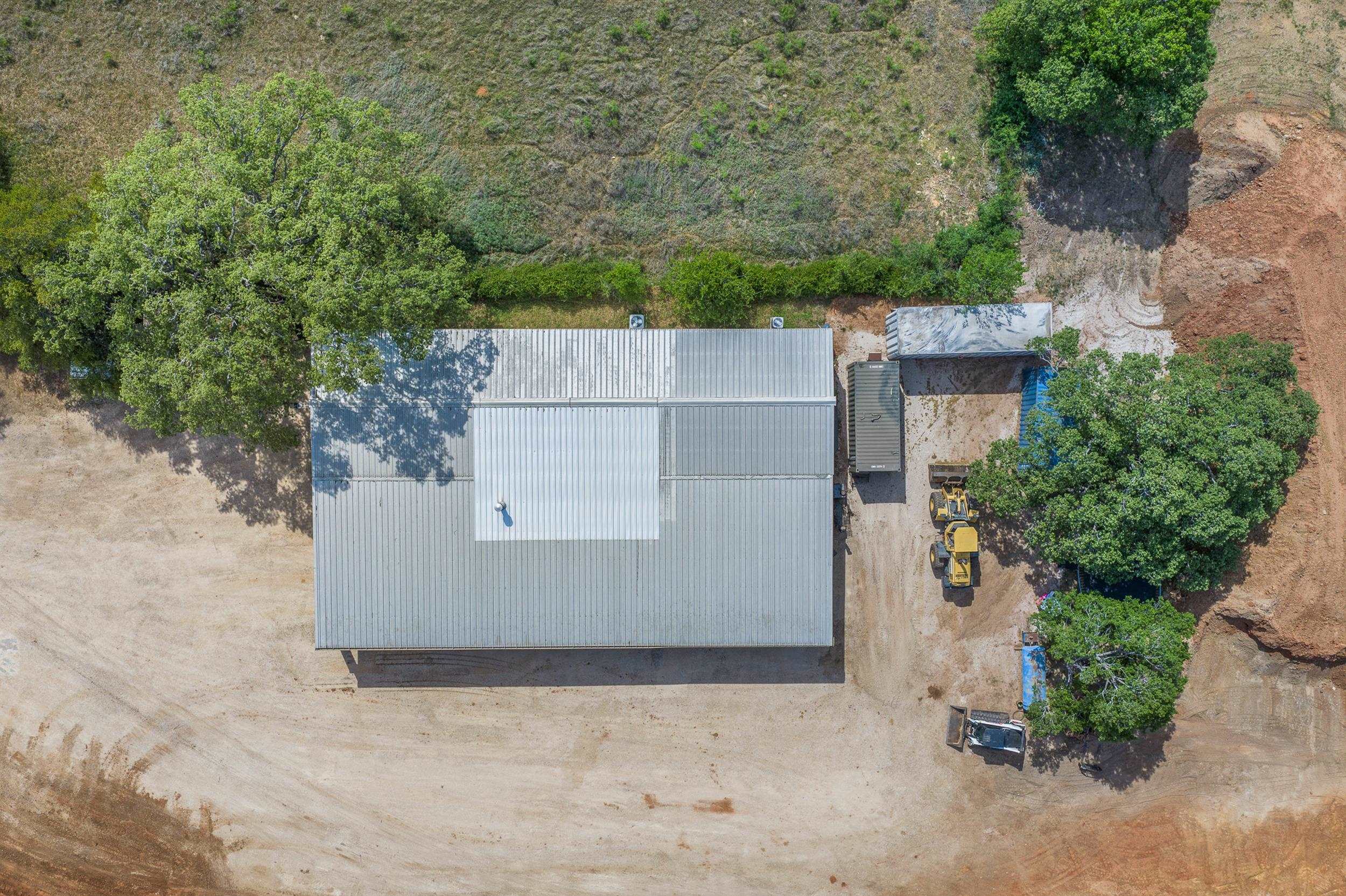 Aerial view of a metal-roofed building, cleared yard, trees, and construction equipment.