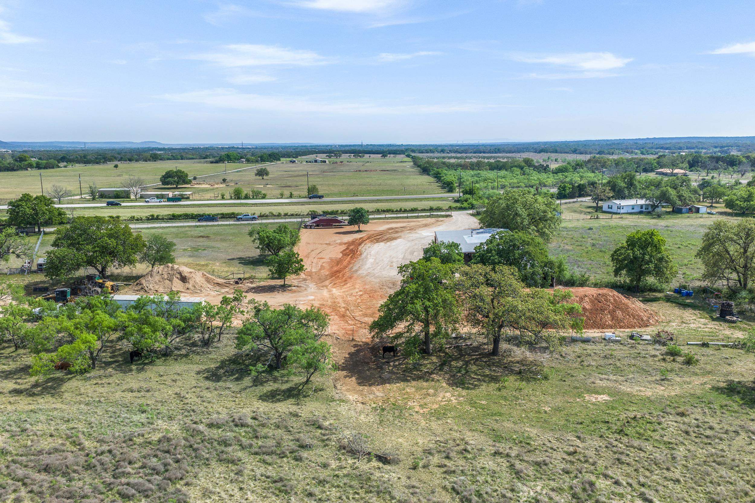 Aerial view of rural acreage with a broad dirt clearing, scattered trees, small buildings, and cattle.