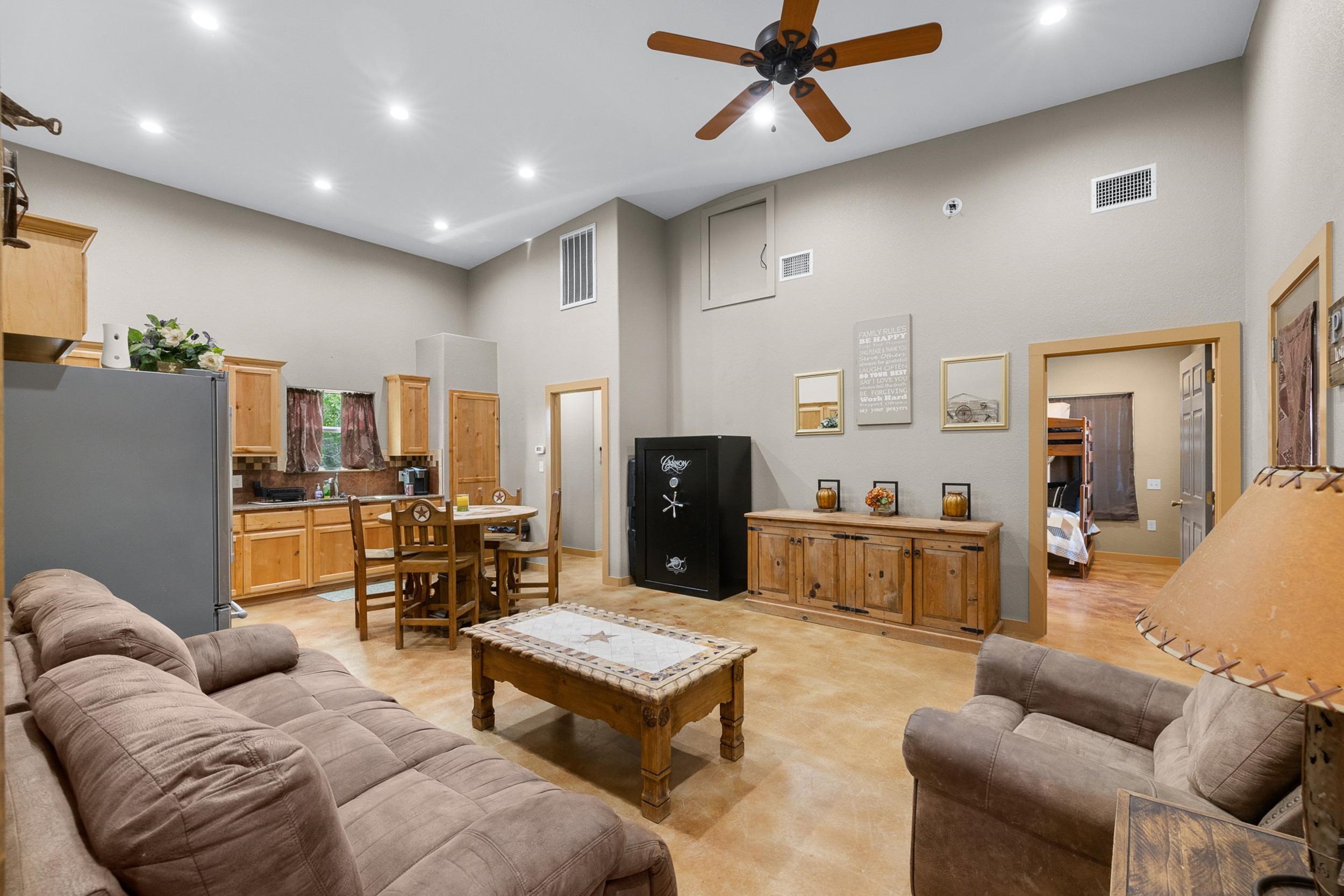 Open-plan living and dining area with wood cabinetry, two sofas, and a ceiling fan.