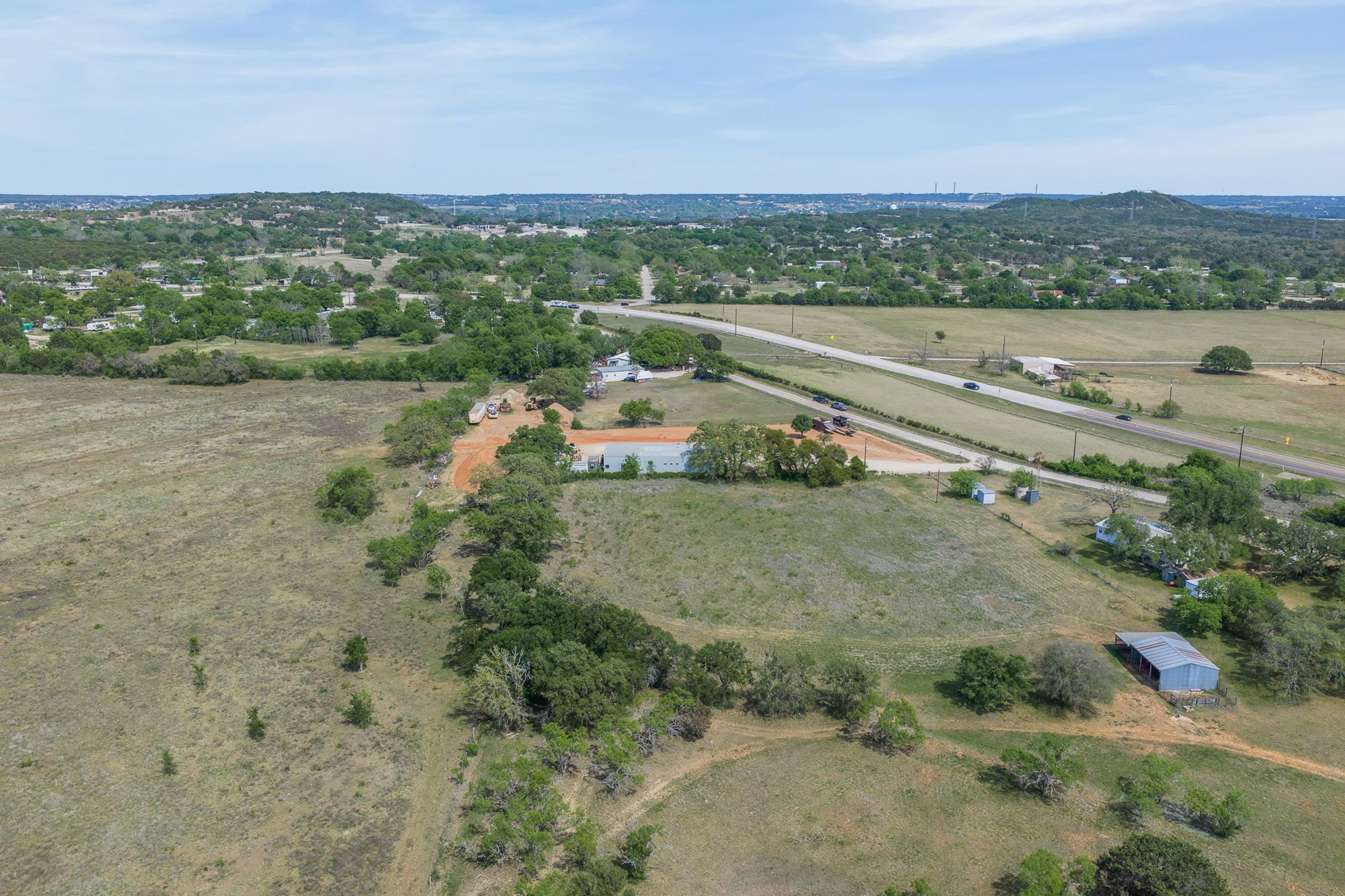 Aerial view of open acreage with scattered trees, outbuildings, and a highway nearby.