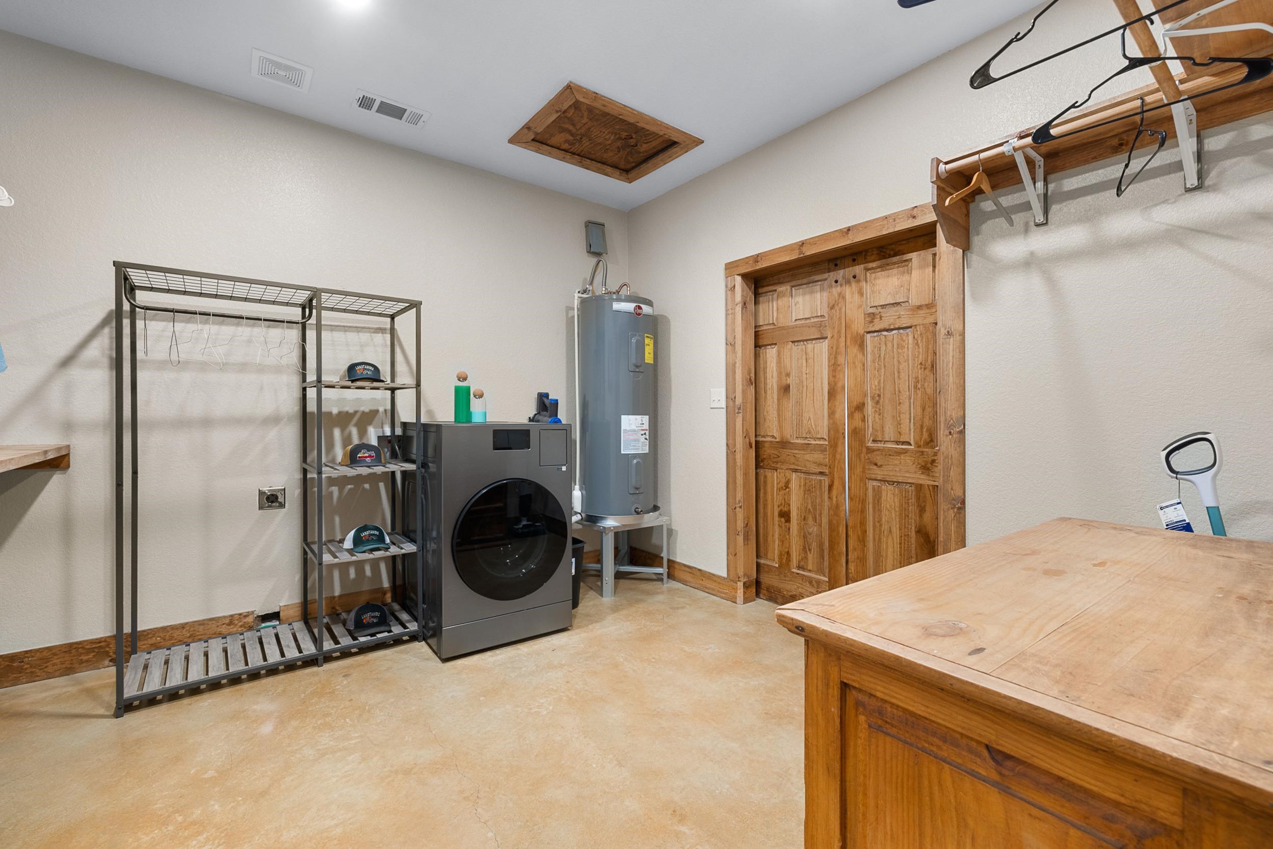 Laundry and utility room with a front-loading washer, water heater, storage rack, and large wooden worktable.