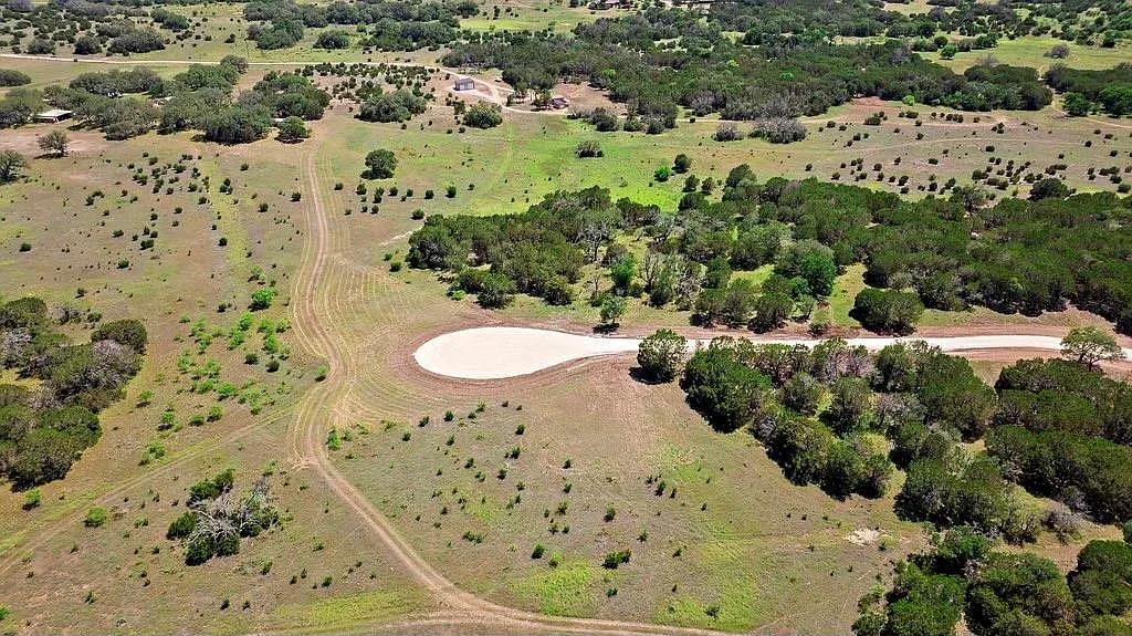 Aerial view of rural acreage with scattered trees and a long pale gravel turnaround.