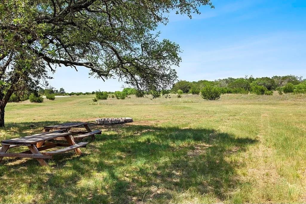 Open grassy acreage with a shaded picnic table and low circular stone fire pit.