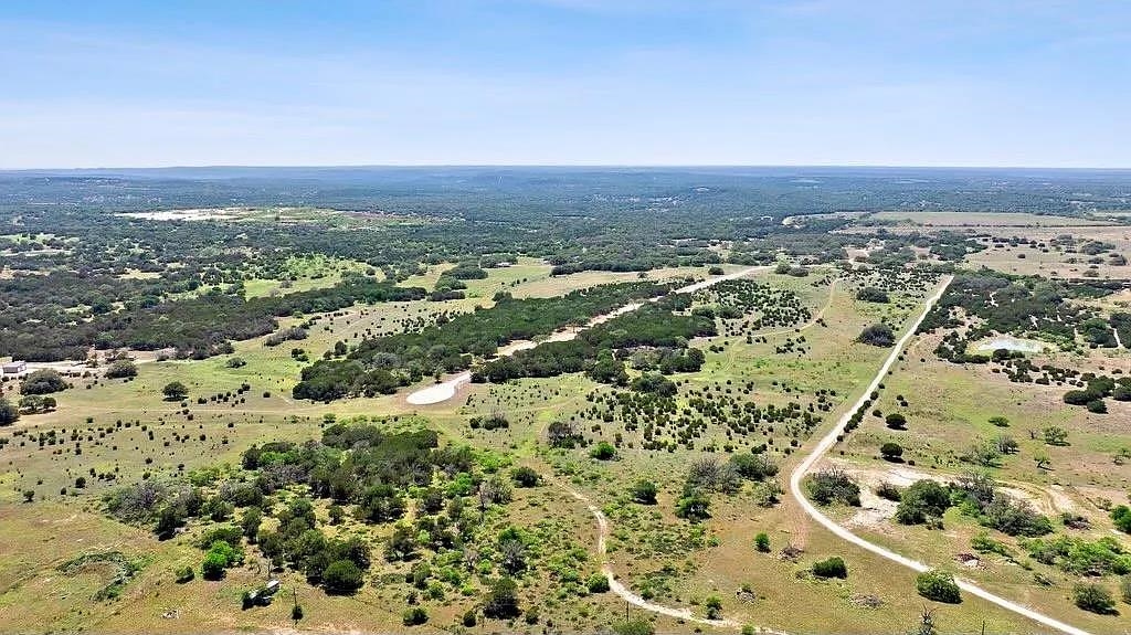 Aerial view of tree-dotted Texas pasture, a winding dirt road, and a small pond.