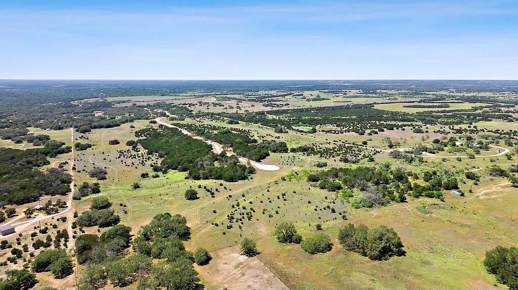 Aerial view of open rural acreage with scattered trees, wooded areas, and dirt roads.