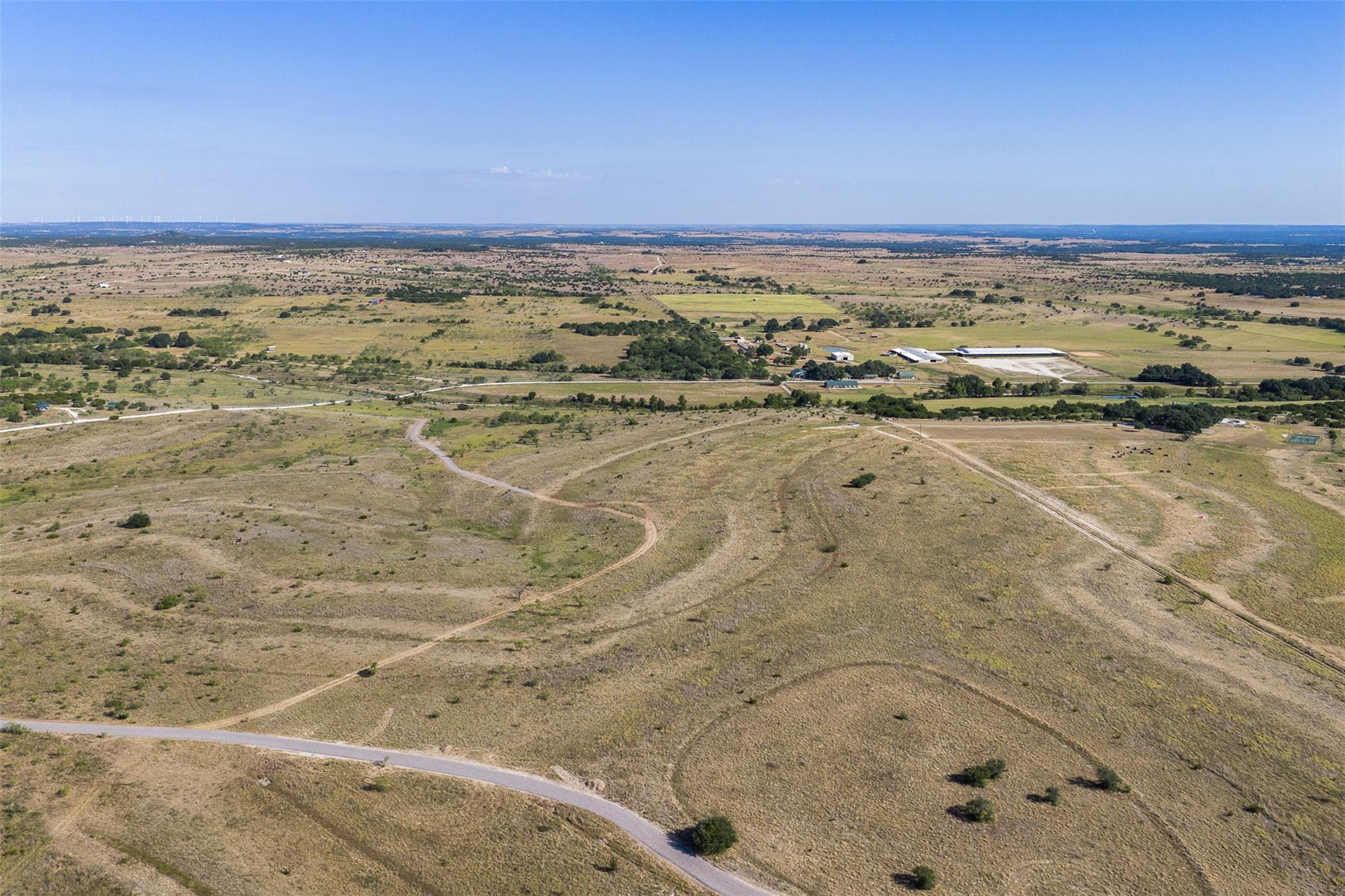 Aerial view of open rural acreage with winding tracks, a paved road, and distant farm buildings.