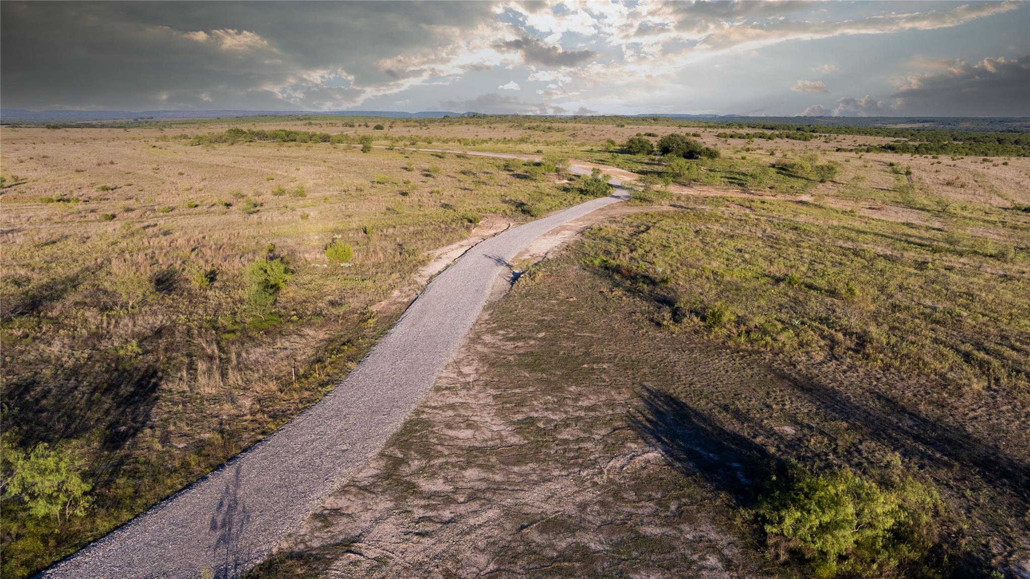 Aerial view of undeveloped land with a gravel road winding through sparse scrub.