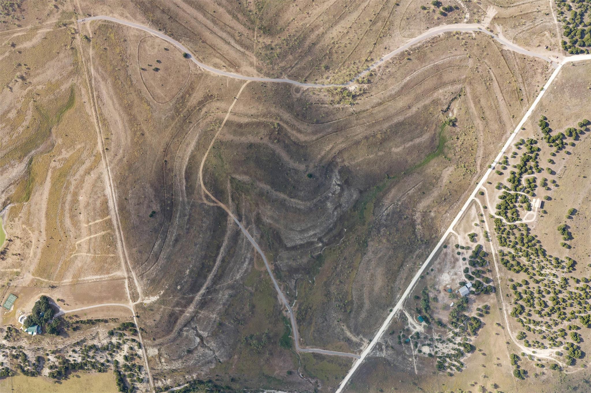 Aerial view of rolling scrubland with winding access roads and scattered neighboring buildings.