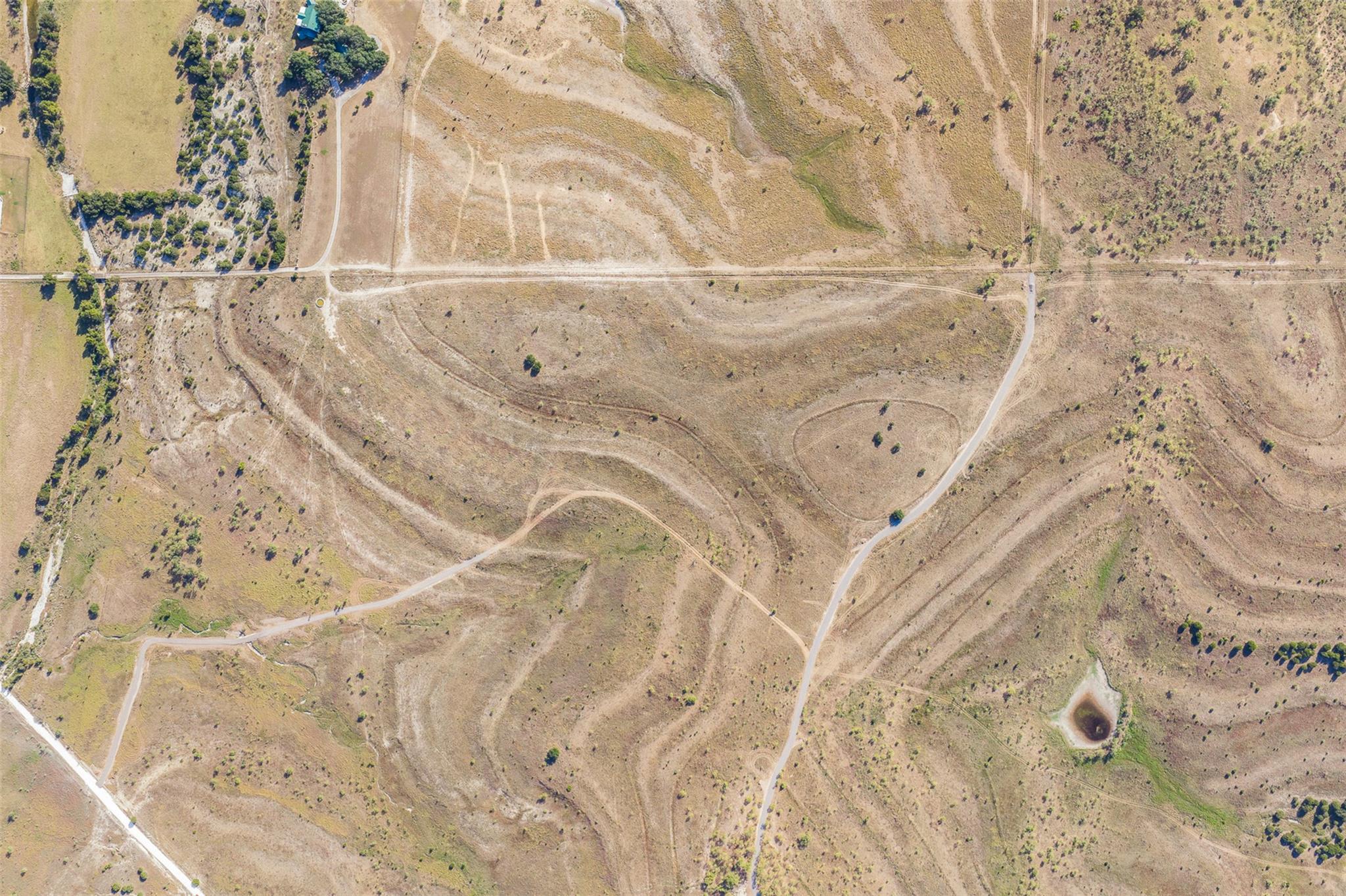 Aerial view of dry rural acreage with winding roads, sparse vegetation, and a small pond.