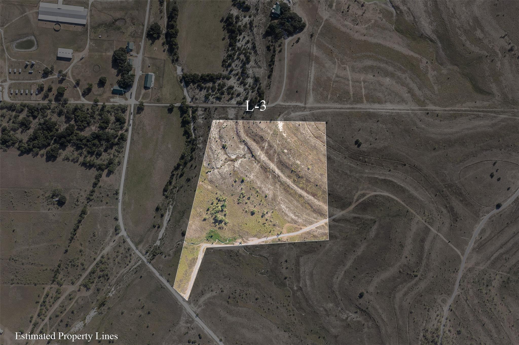 Aerial view of vacant Lot L-3 outlined by estimated property lines, with sparse brush and a dirt access road.