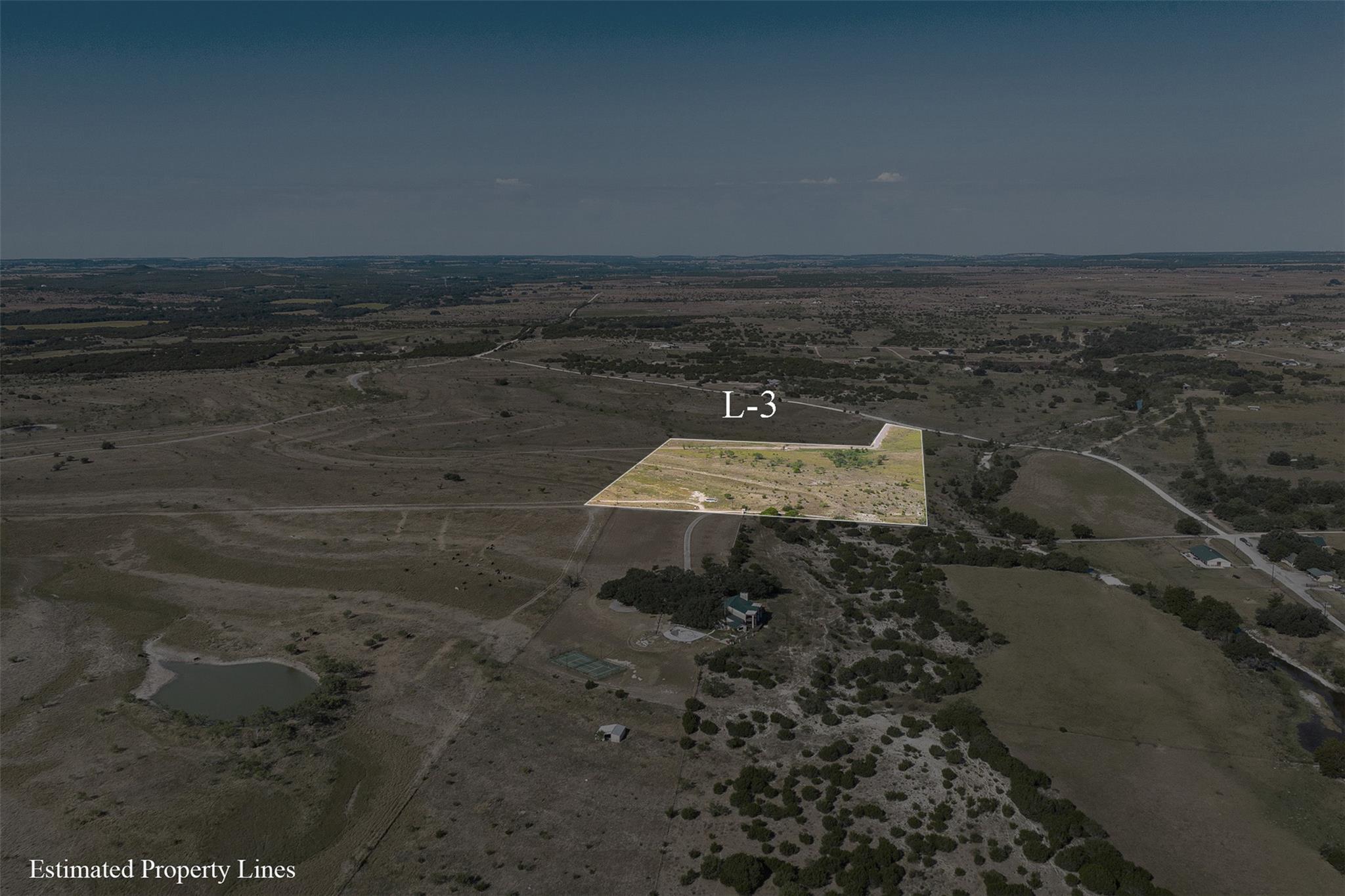 Aerial view of vacant Lot L-3, outlined amid rural scrubland near scattered homes and a small pond.