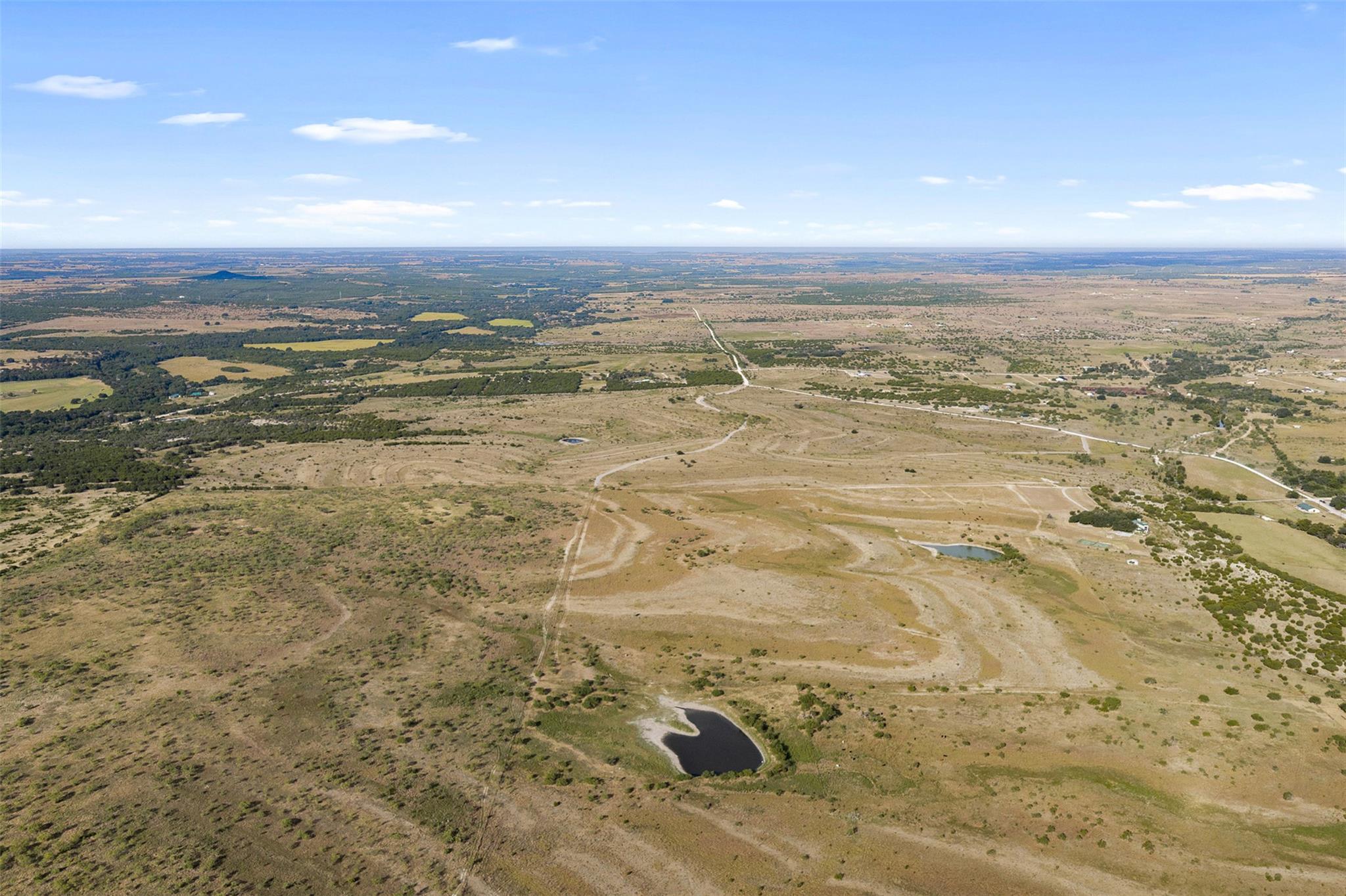 Aerial view of open rural acreage with winding dirt roads and several ponds.